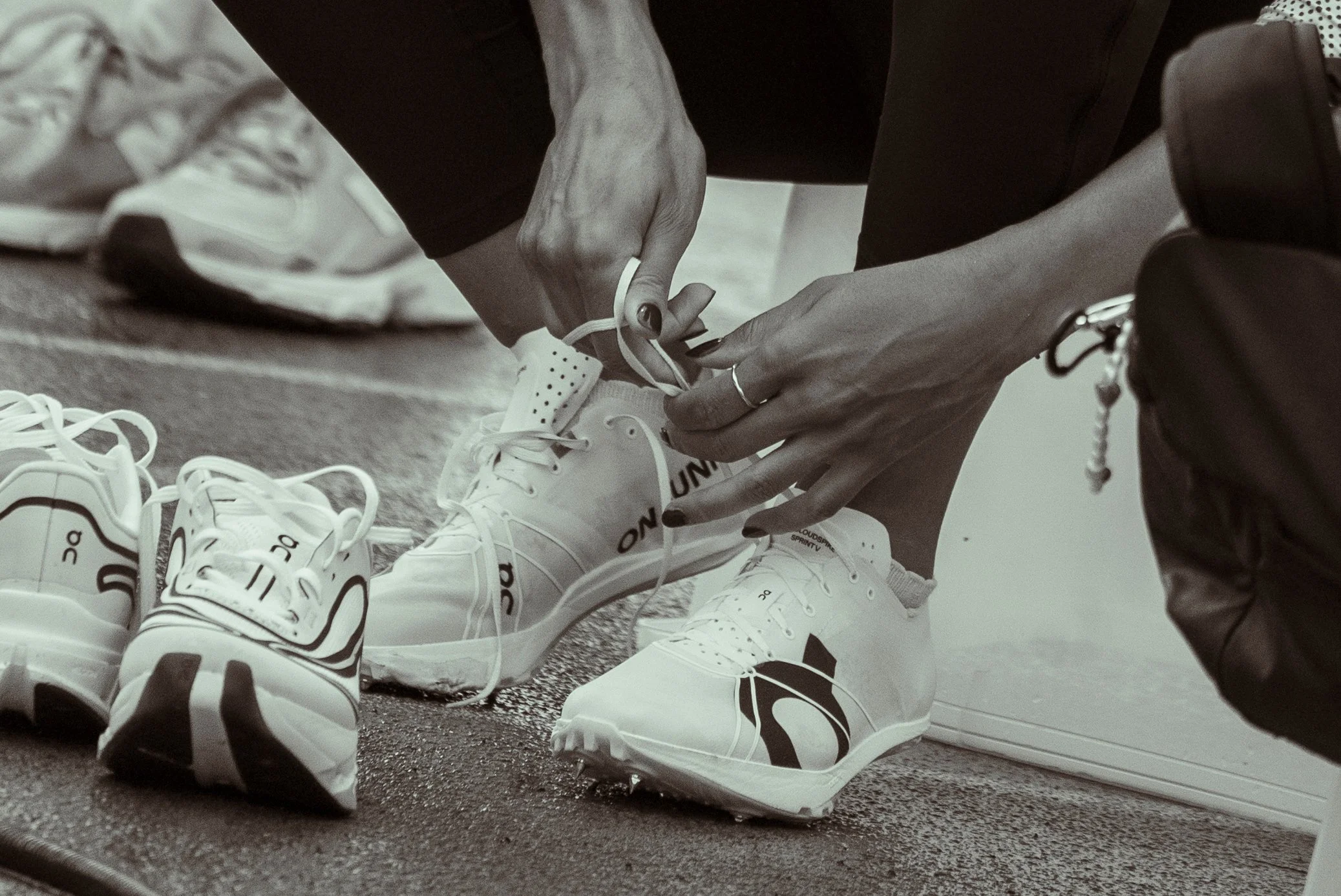 Person tying shoelaces on multiple pairs of white sneakers in a room.