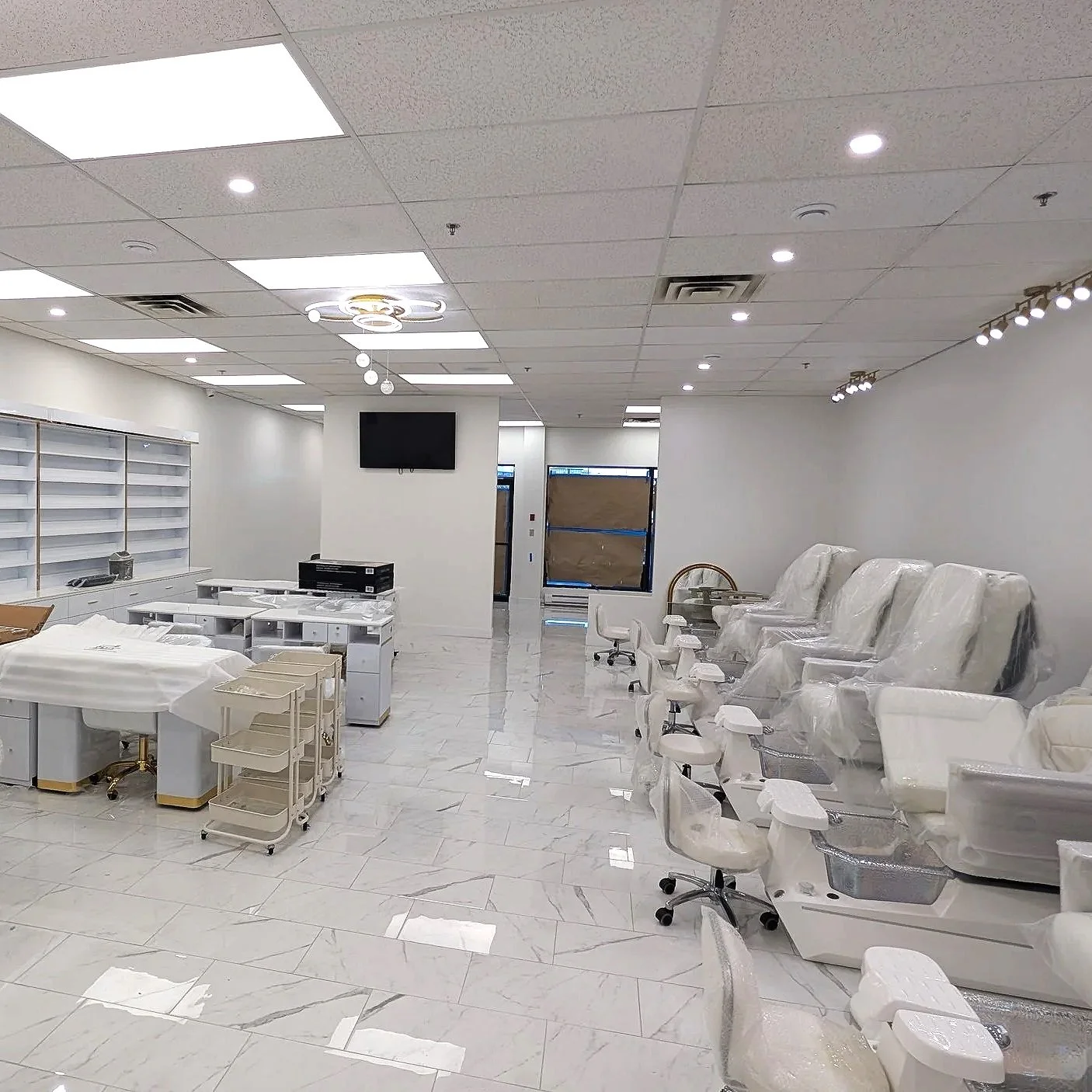Unfinished nail salon with white decor, chairs covered in plastic, and shelves for nail polish displays.