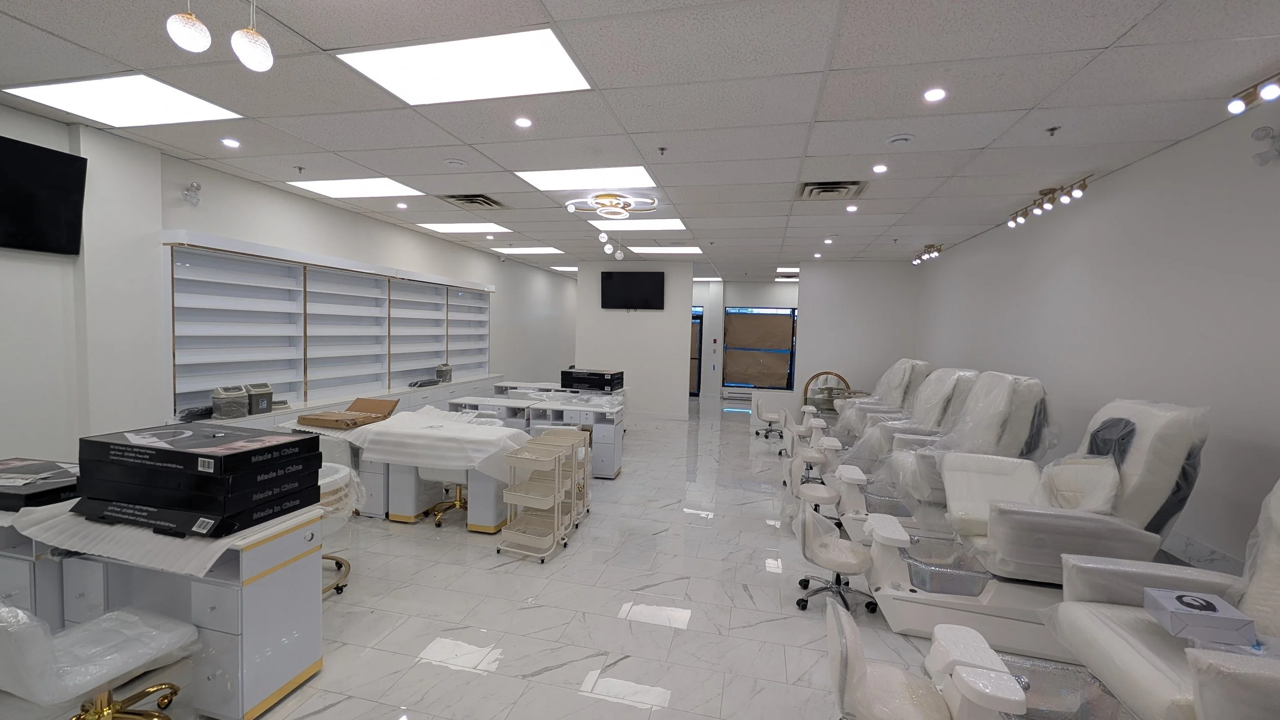 Interior of a new or renovated medical clinic or office, with white walls and furniture, some covered in protective plastic, and shelves on the wall, possibly for patient storage or display.