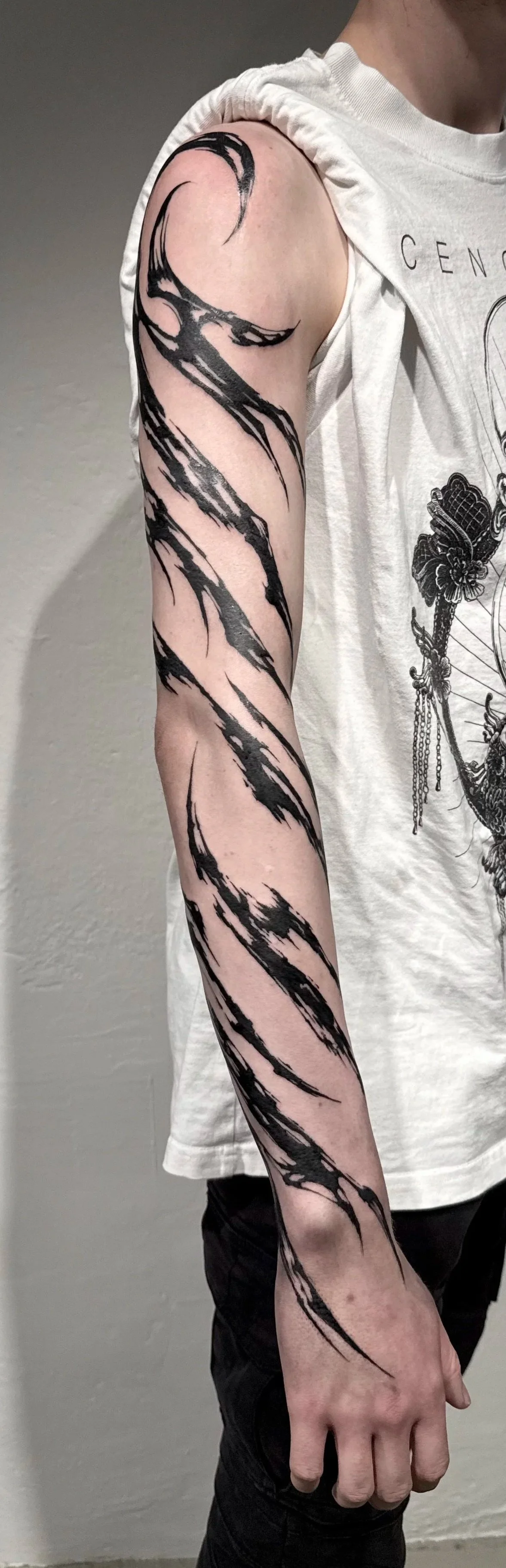Tattoo eines schwarzen, kratzartigen Musters auf dem linken Arm einer Person.
