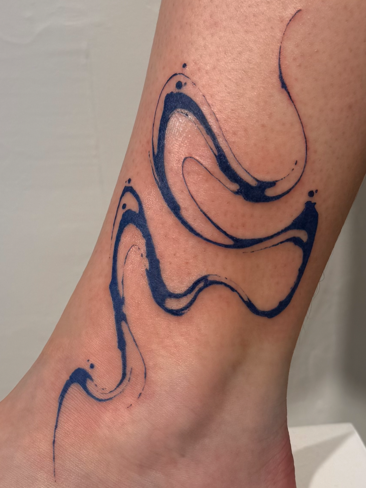 Tattoo eines abstrakten, wellenförmigen Designs in dunkler blauer Farbe auf der Wade einer Person.