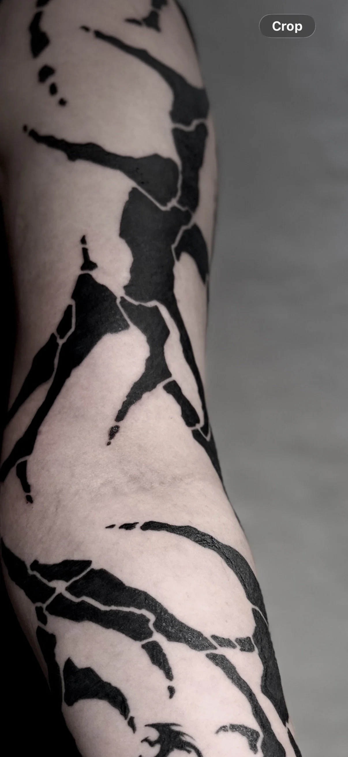 Schwarze Tribal-Tattoo auf hellhäutigem Unterarm, abstraktes Design mit Linien und Flächen.