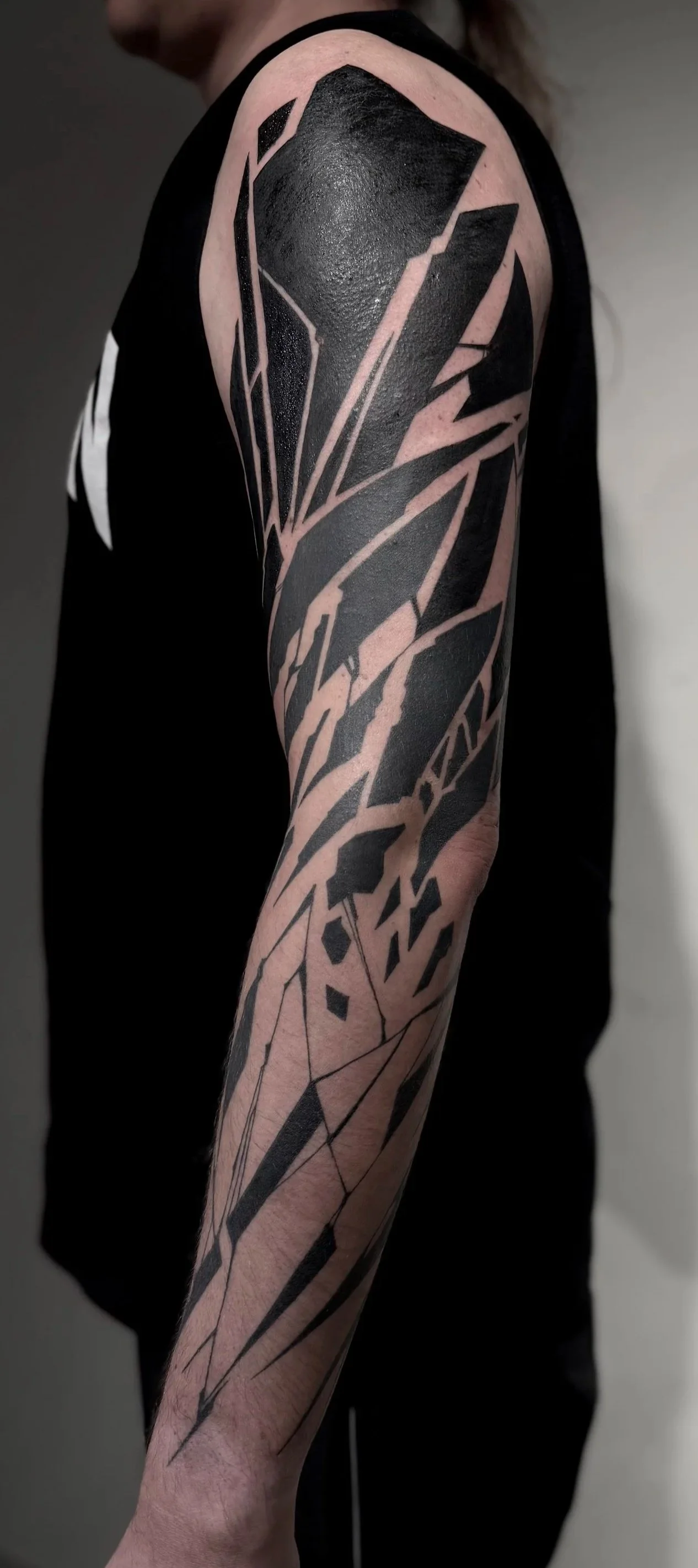 Schwarzes geometrisches Tattoo auf einem Arm, bestehend aus Linien und stikartigem Design.