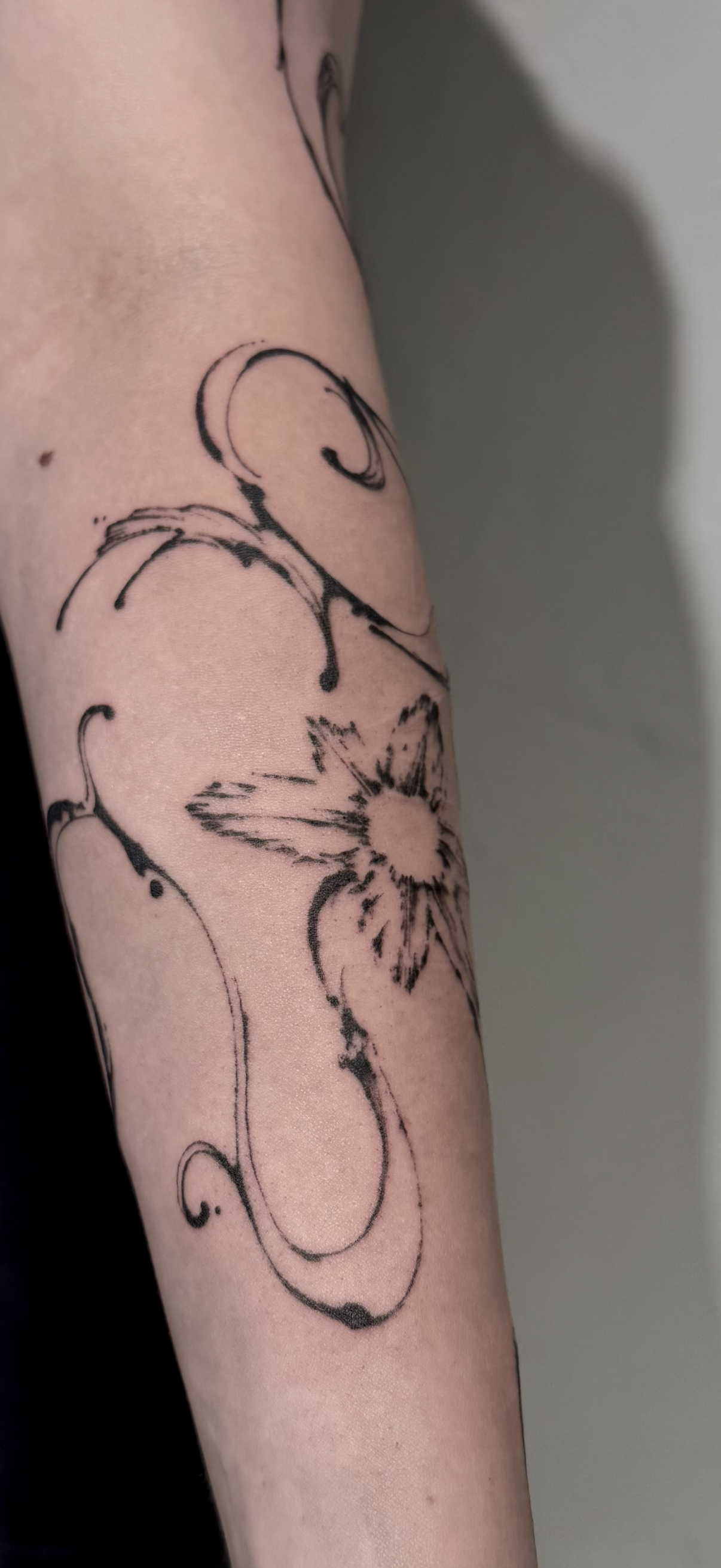 Tattoo eines Blumenmotivs auf einem Arm, in Skizzenstil mit schwarzen Linien und fluider Formern.