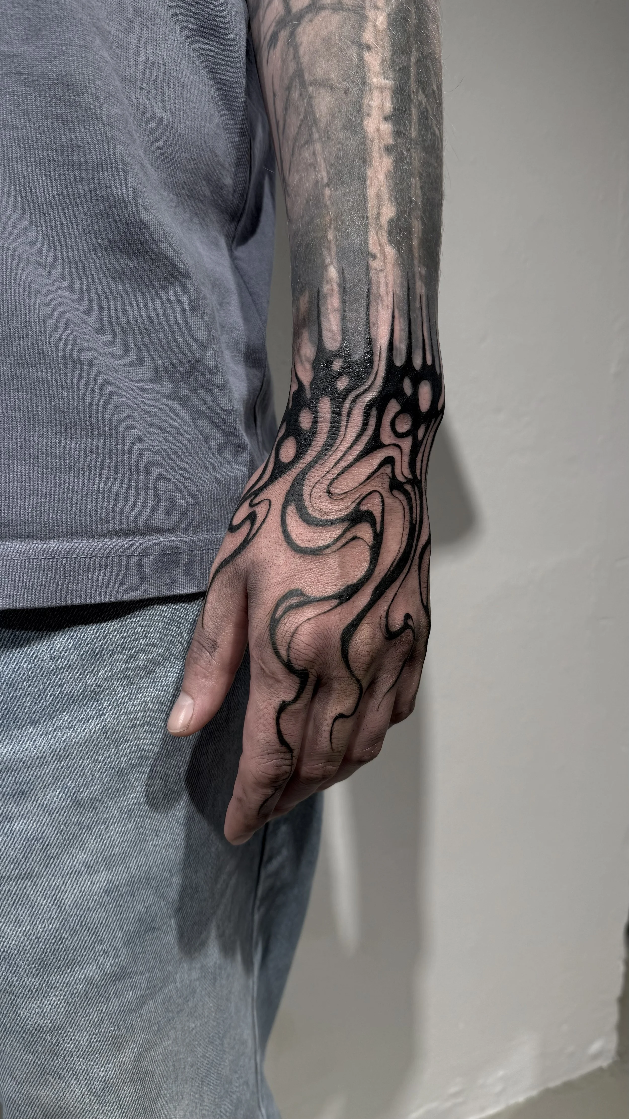 Der Arm einer Person ist tätowiert mit einem schwarzen und rosa abstrakten, fließenden Design, das sich vom Handgelenk bis zum Oberarm erstreckt.