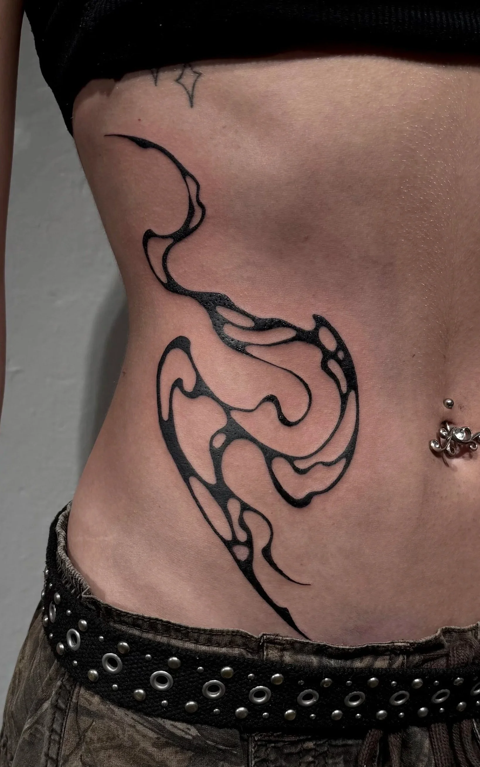 Schwarzes tribalartiges Tattoo an der Seite des Bauches einer Person.