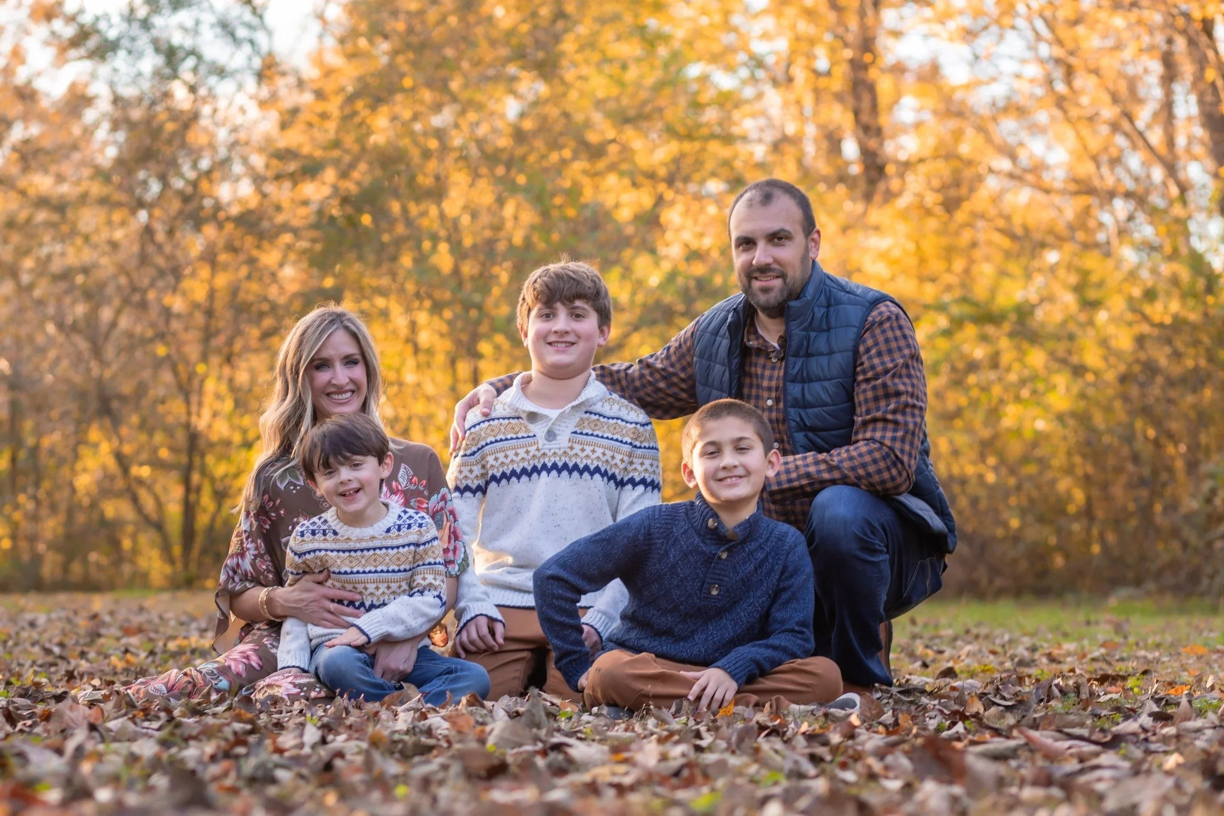 Family of five sitting together in fall leaves at Aspen Grove Park in Franklin, TN