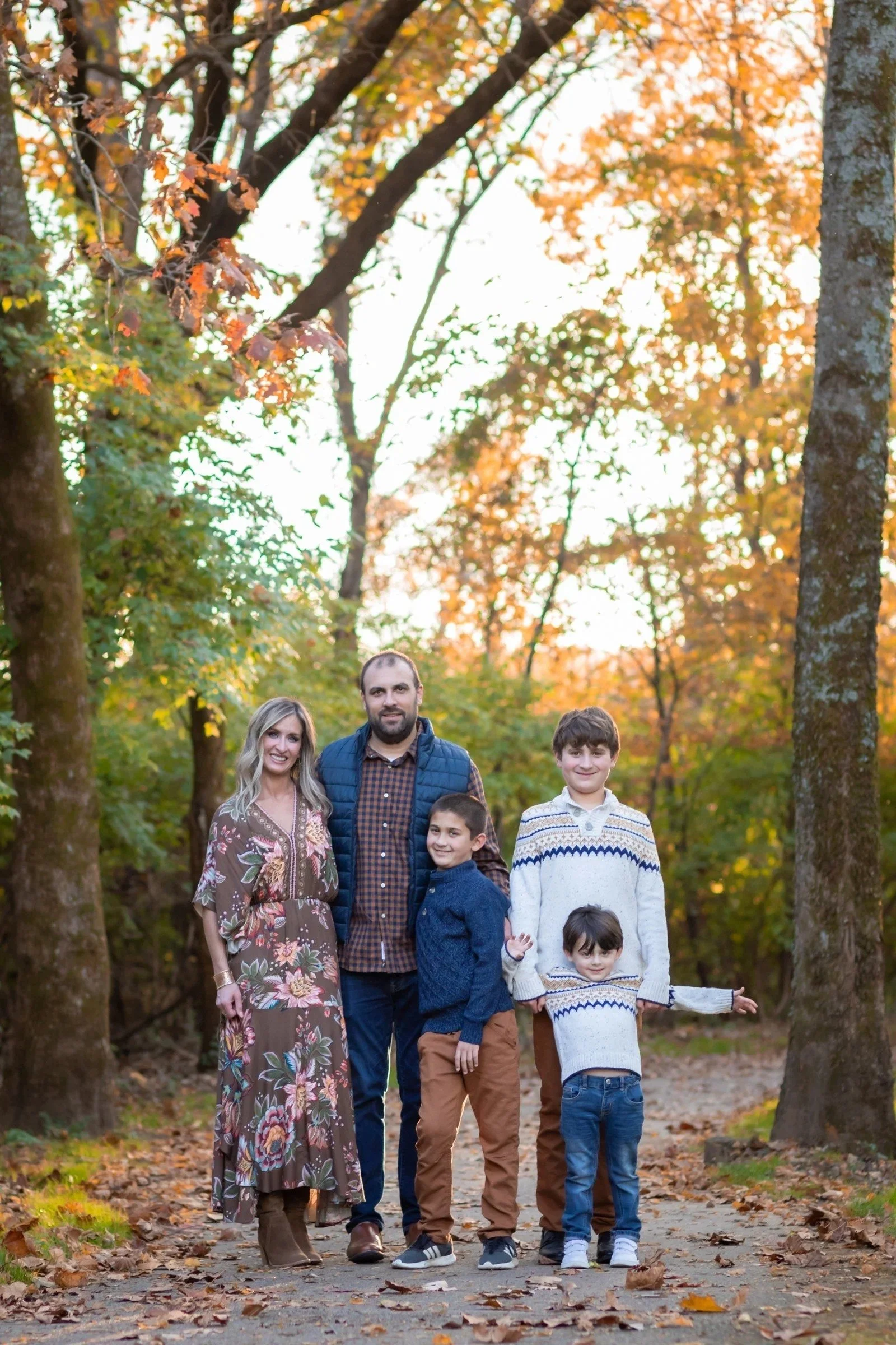 Family of five under tall autumn trees in late-day light