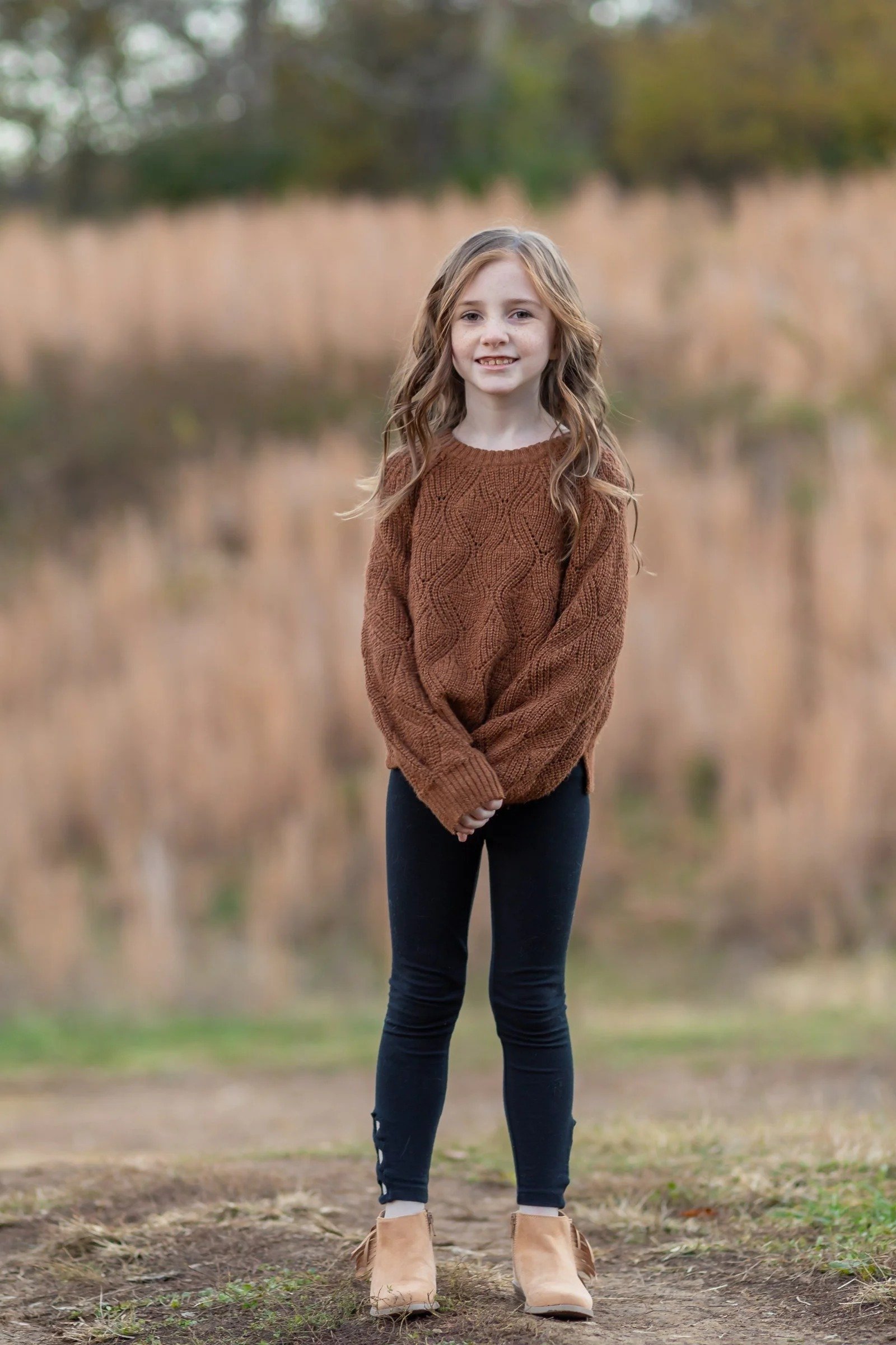 Girl in a brown sweater standing in front of tall golden grass