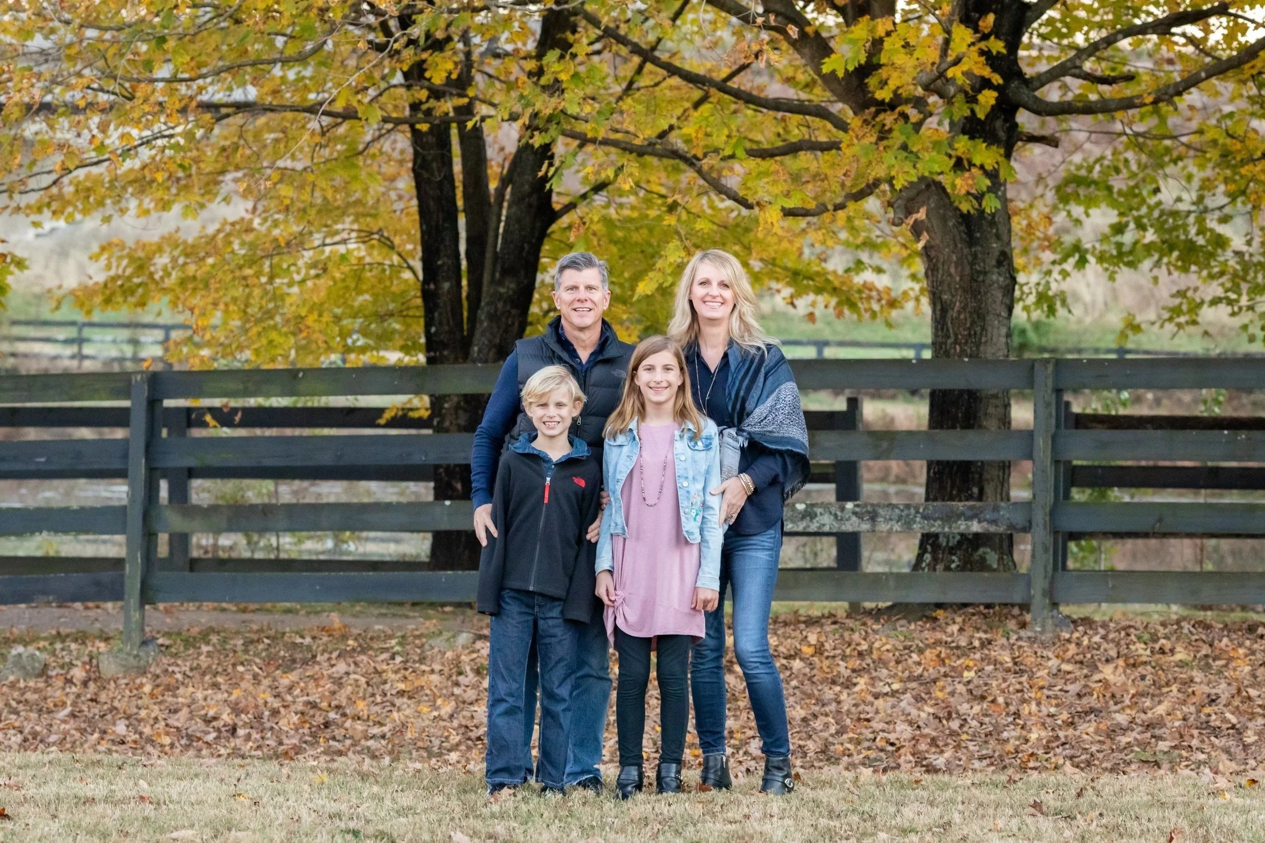 Family of four by a wooden rail fence under fall trees at Smith Park in Brentwood, TN