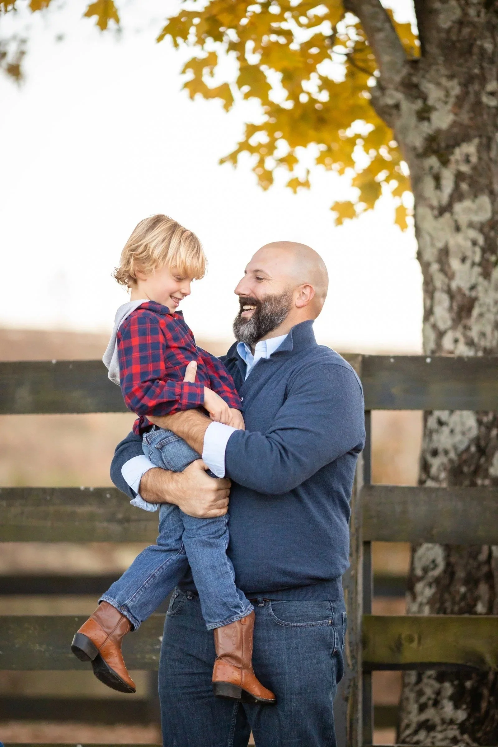 Father holding his young son by a wooden fence under fall leaves