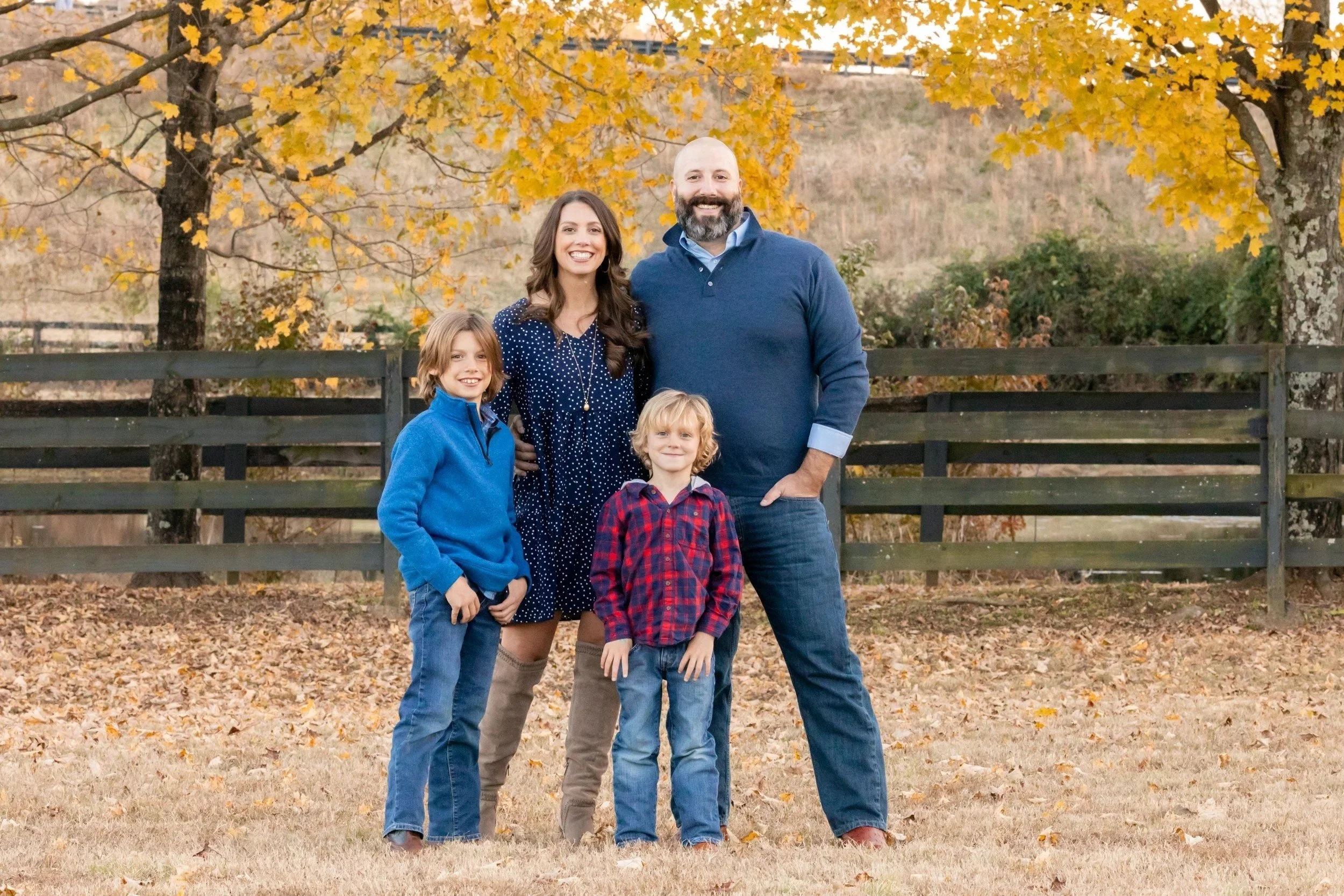 Family of four by a wooden fence under yellow fall trees at Smith Park in Brentwood, TN