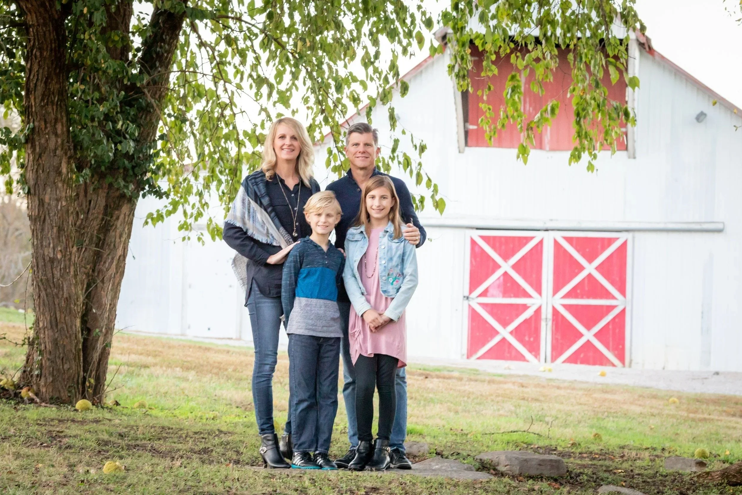 Family of four in front of the white barn with red doors at Smith Park in Brentwood, TN