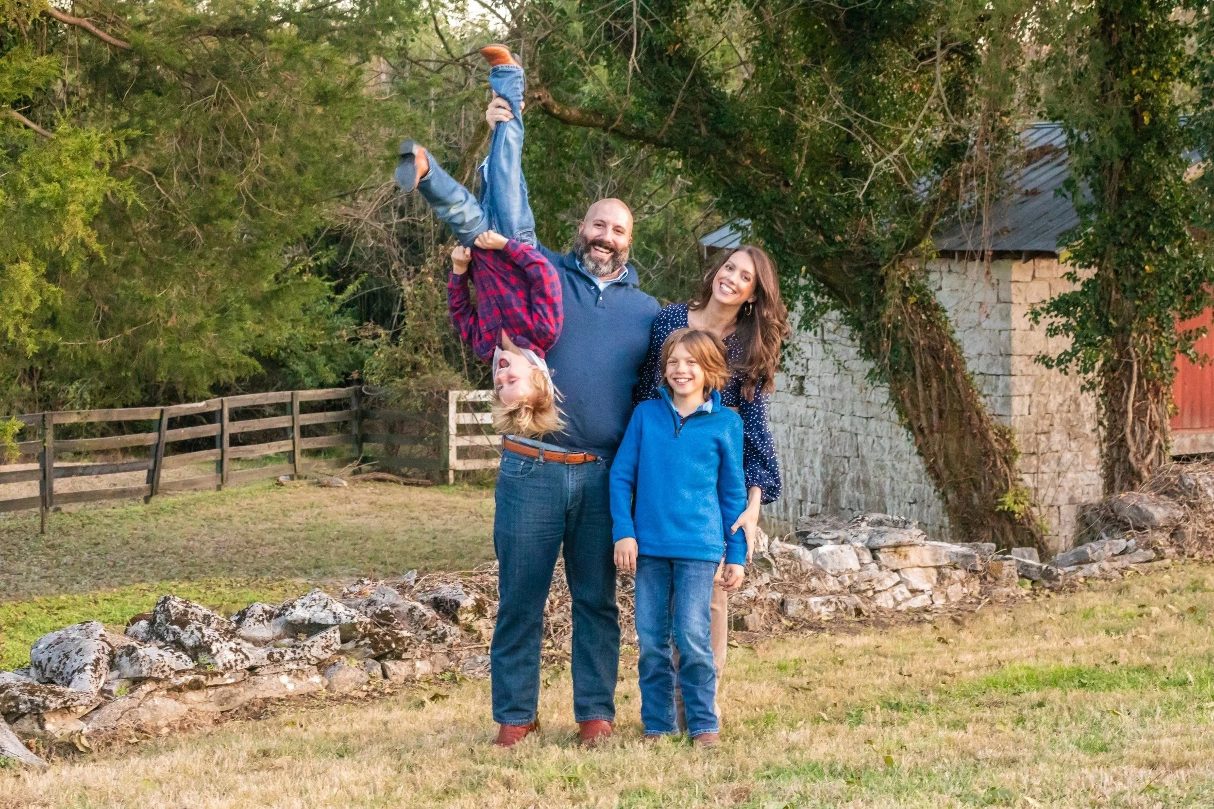 Playful family of four, dad lifting his son, beside the old stone building at Smith Park in Brentwood, TN