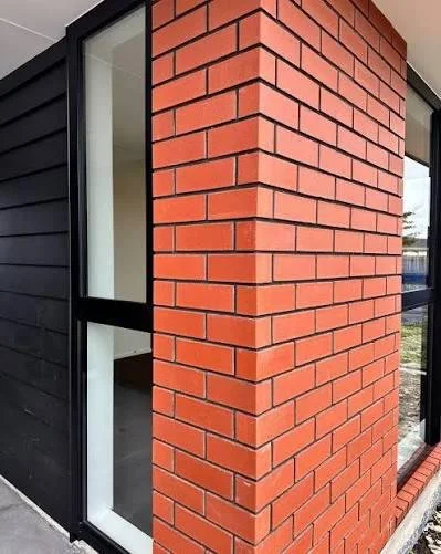 Red brick facade with crisp joints next to dark cladding and glazing.
