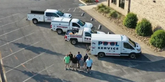 Four pool service trucks parked in a parking lot with a group of six people standing nearby.