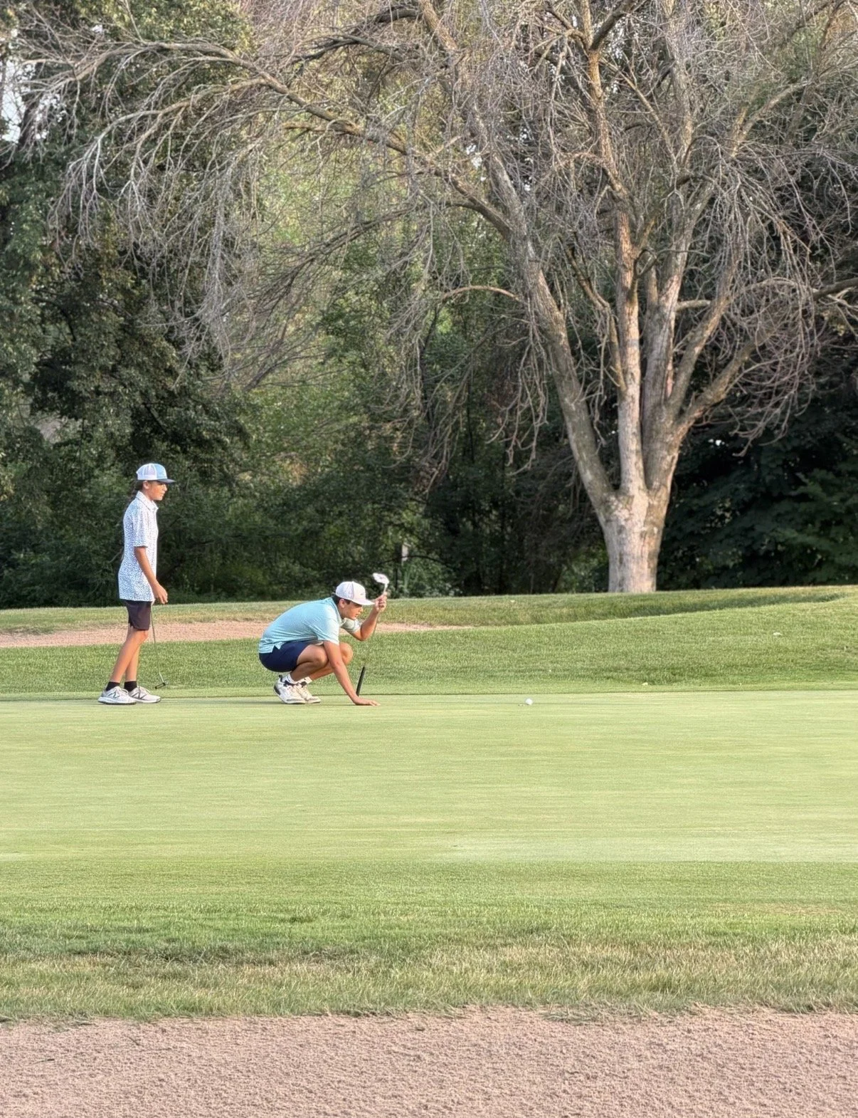 Two junior golfers read a putt together during on-course play.