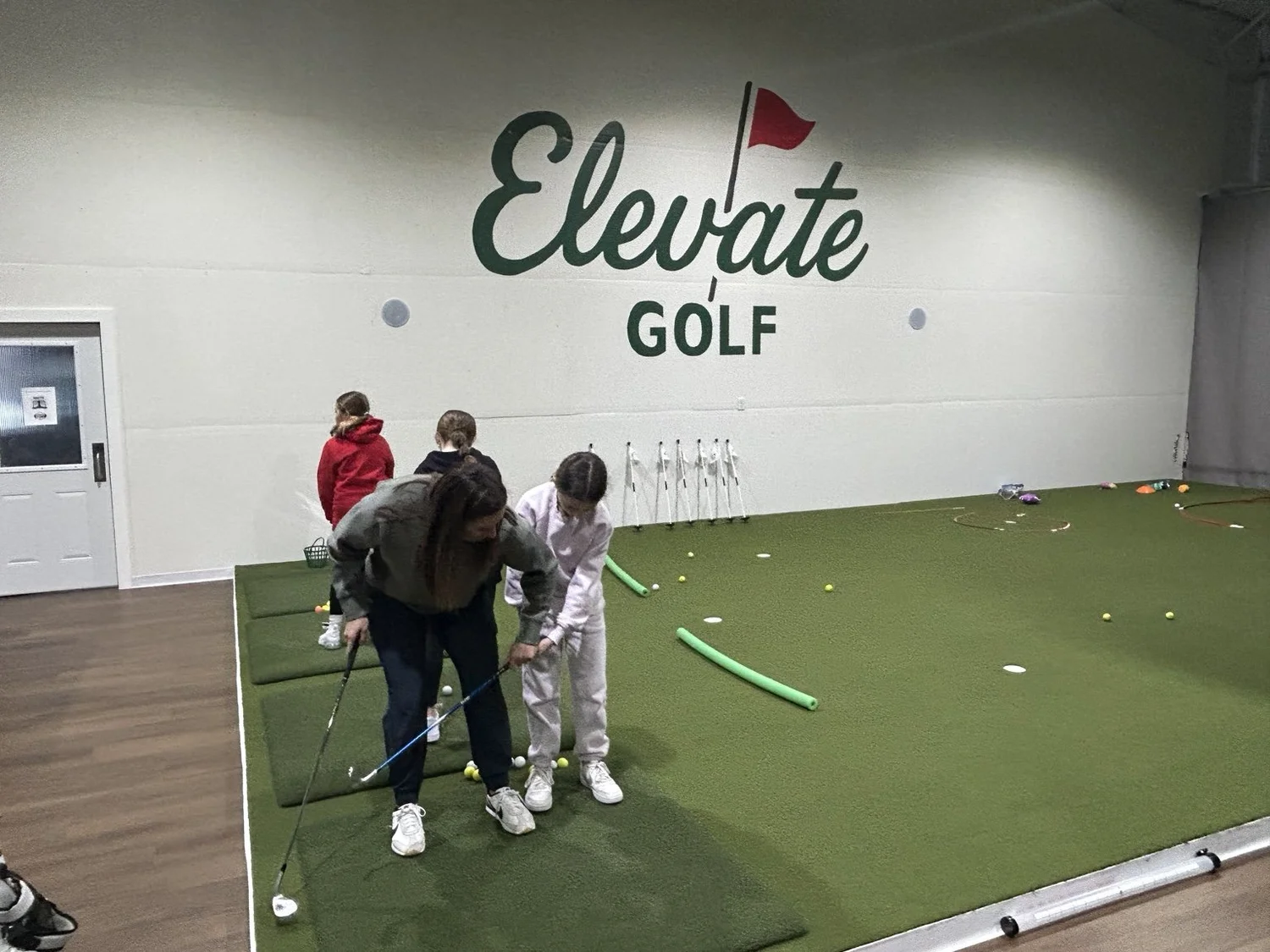 A coach gives a junior golfer hands-on instruction inside Elevate Golf.