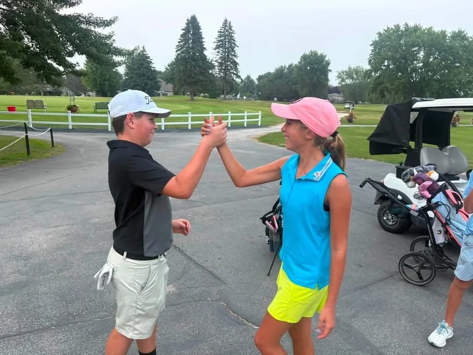 Junior golfers high-five beside their golf bags at a Legends League event.