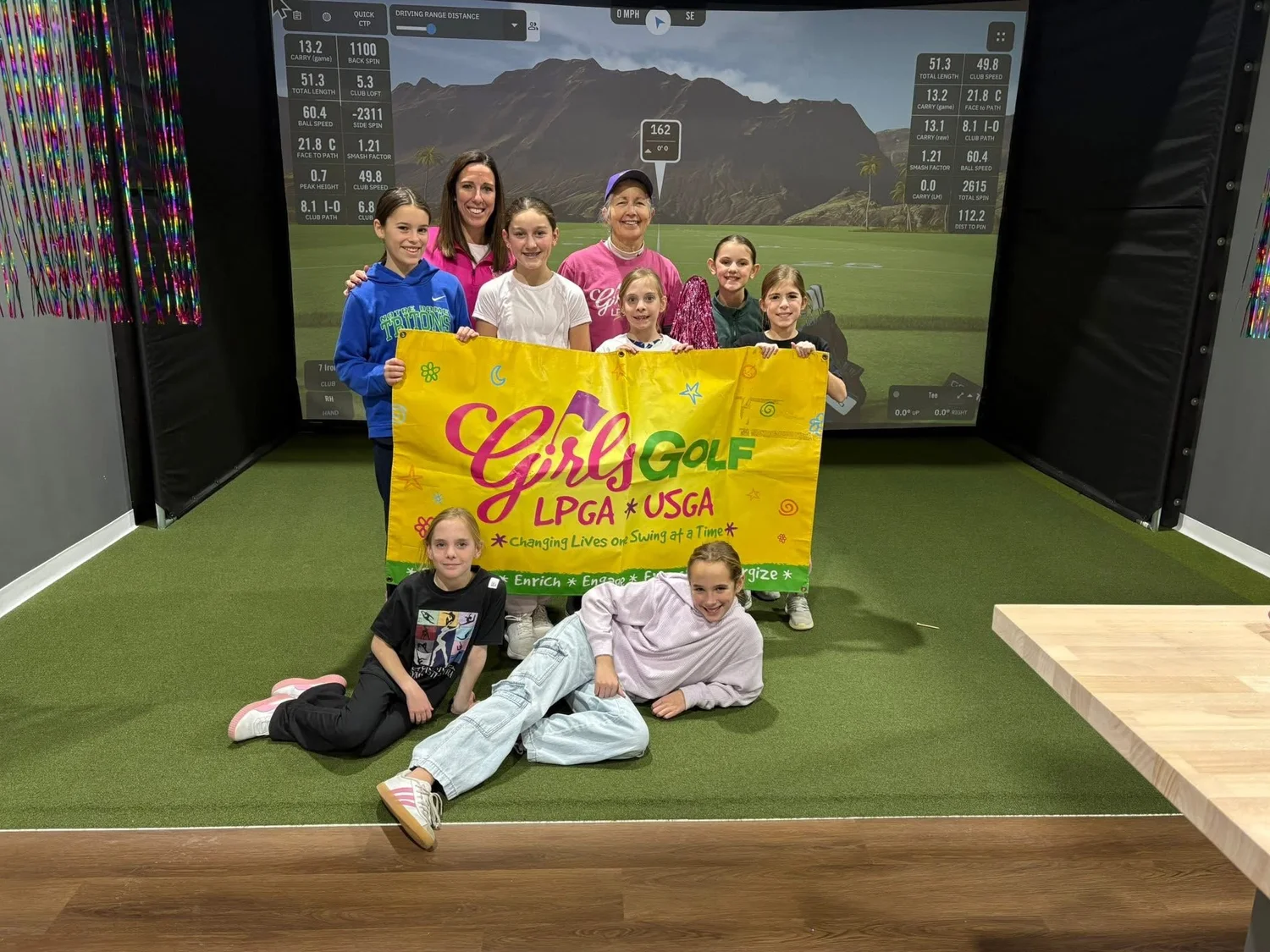 Elevate Girls Golf participants pose with an LPGA Girls Golf banner inside the simulator facility.