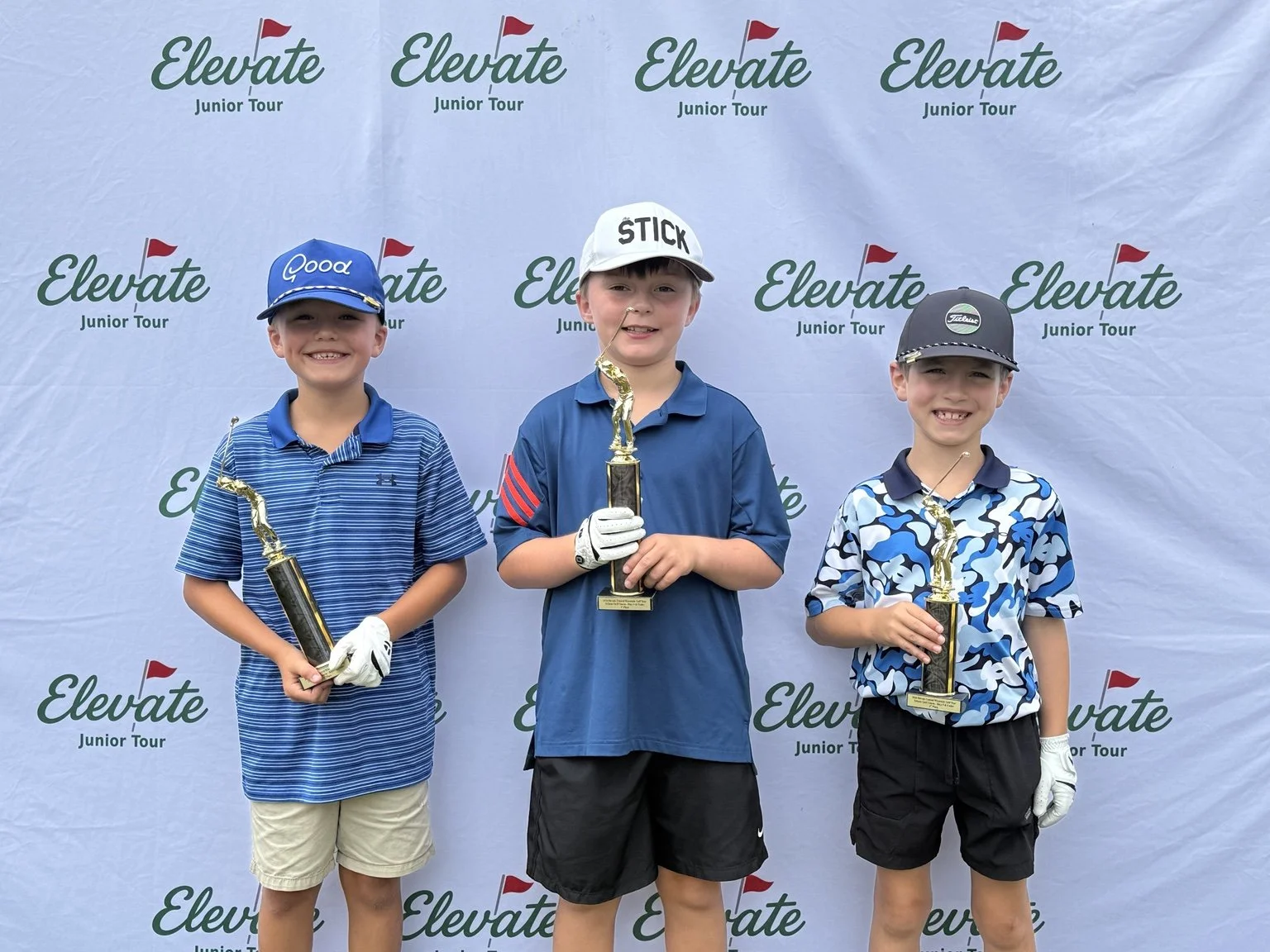 Three Emerging Tour boys hold trophies in front of the Elevate Junior Tour backdrop.
