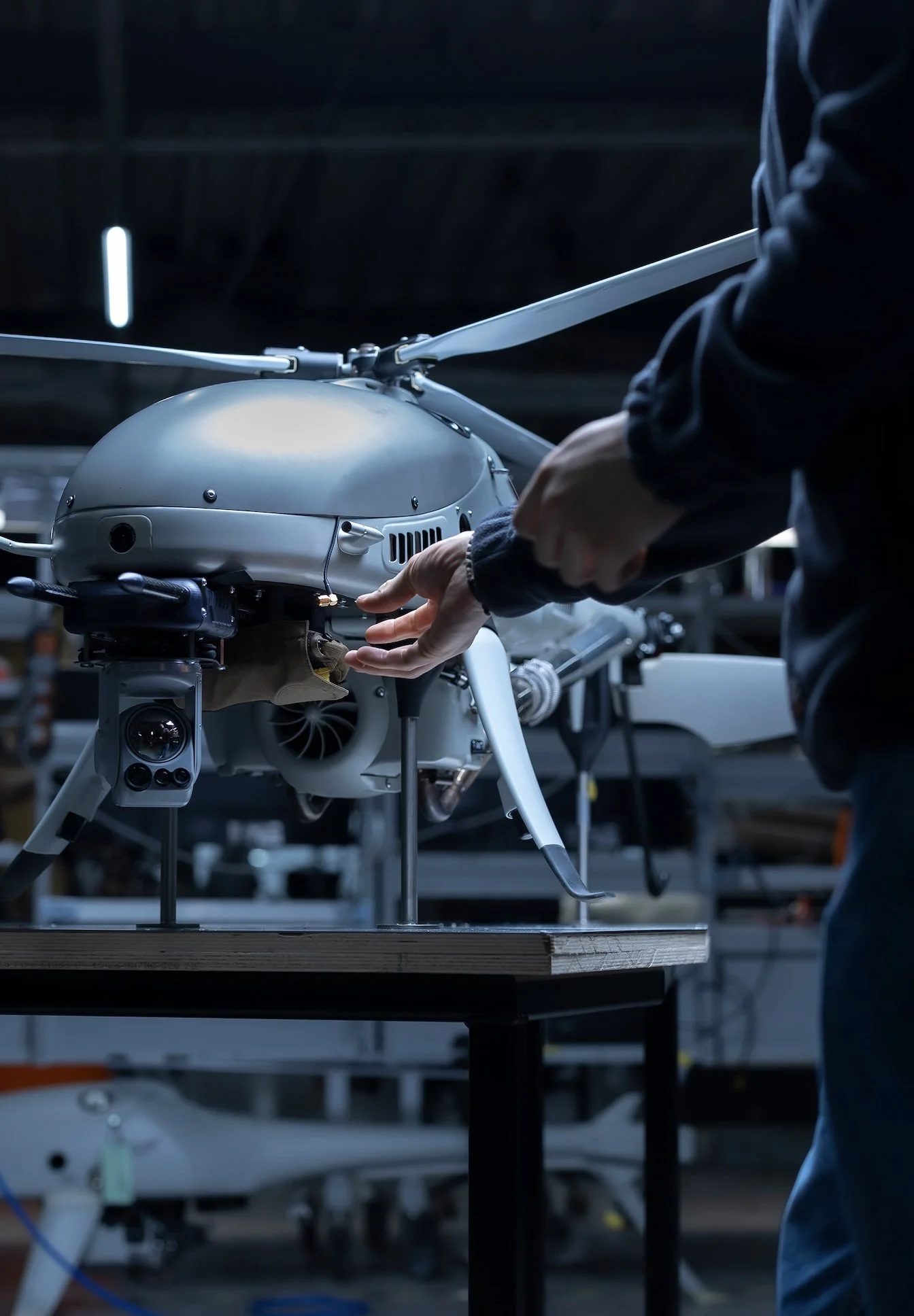 A person working on a drone in a workshop, with tools and equipment visible in the background.