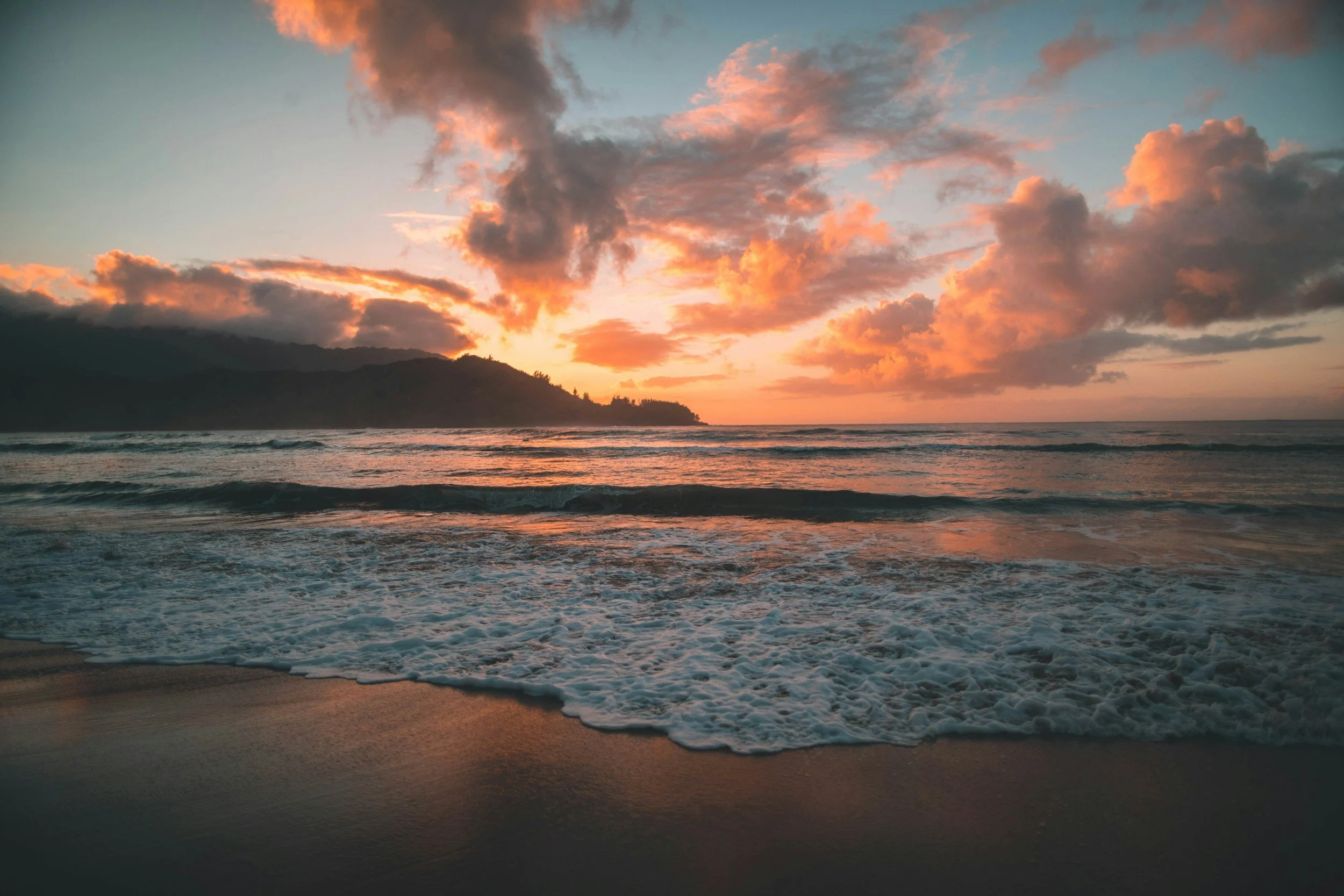 Sunset over the ocean with clouds in the sky and waves on the shore.
