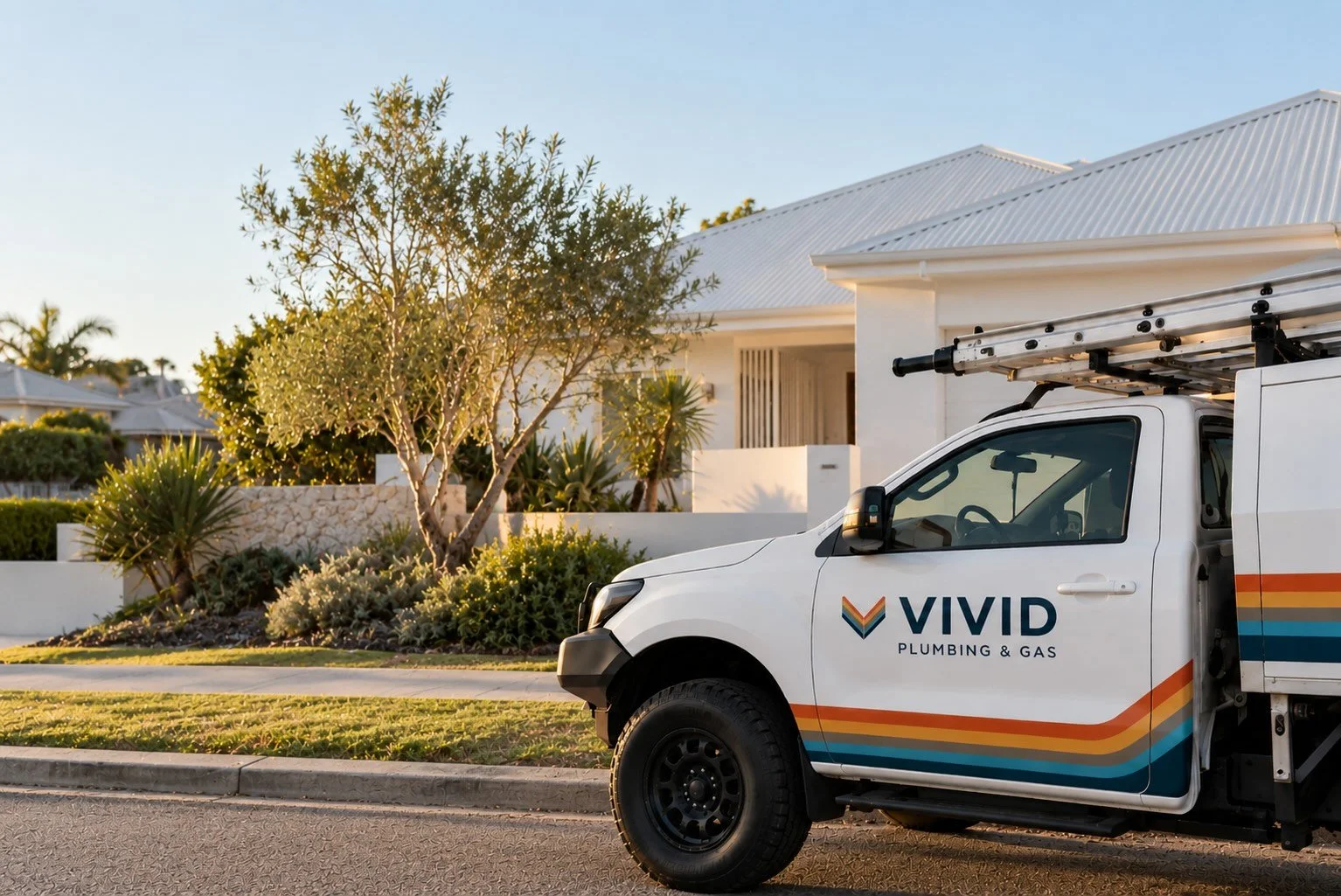 A white service truck with colorful stripes and the logo 'VIVID Plumbing & Gas' parked in front of a modern white house with landscaped yard, a tree, and tropical plants, during daytime.