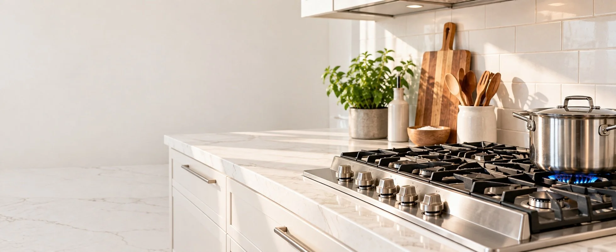 Modern kitchen countertop with a stainless steel pot on a gas stove, a cutting board, potted plant, bottles, and wooden utensils in containers.
