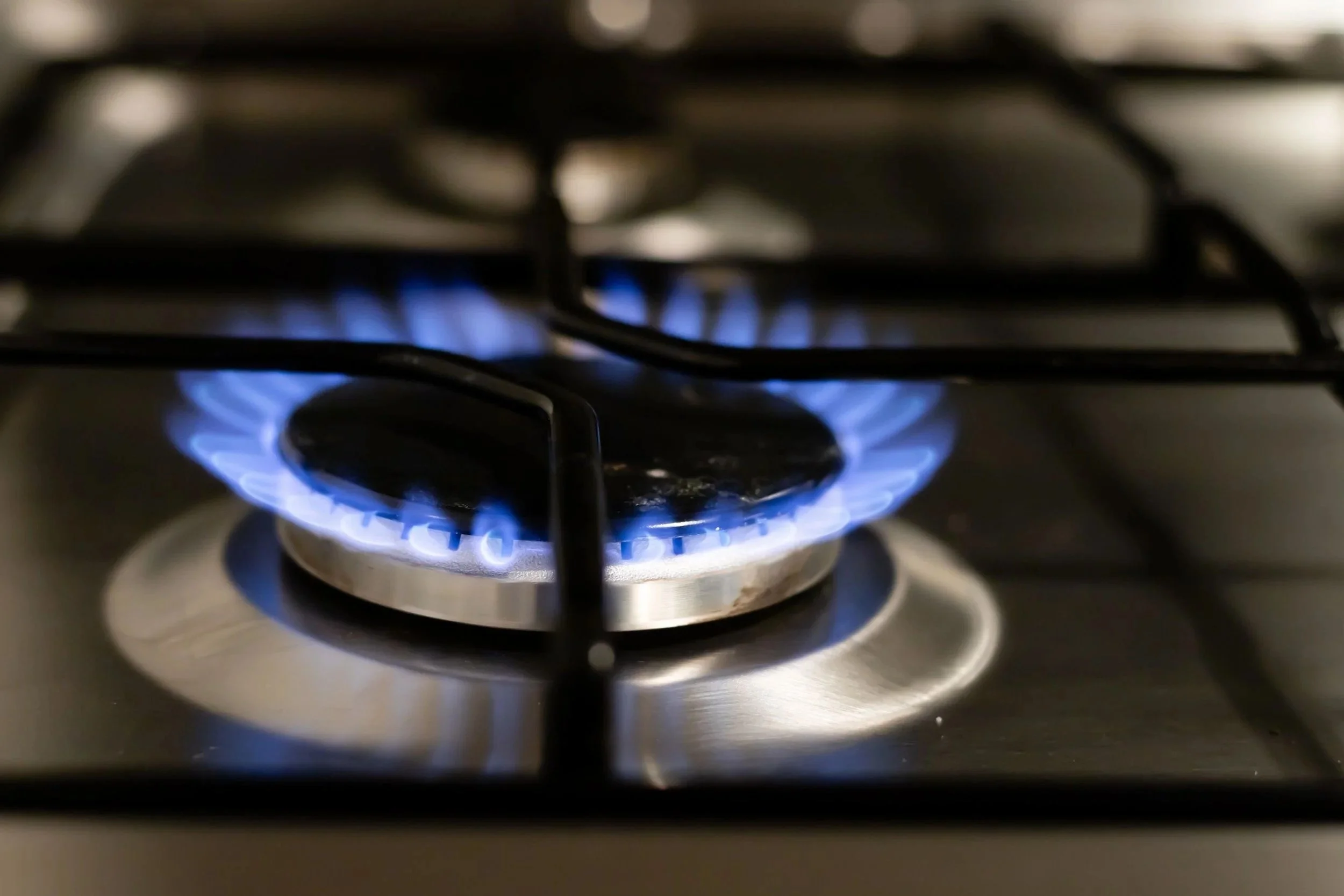 A close-up view of a lit gas stove burner with blue flames surrounding a metal circle.