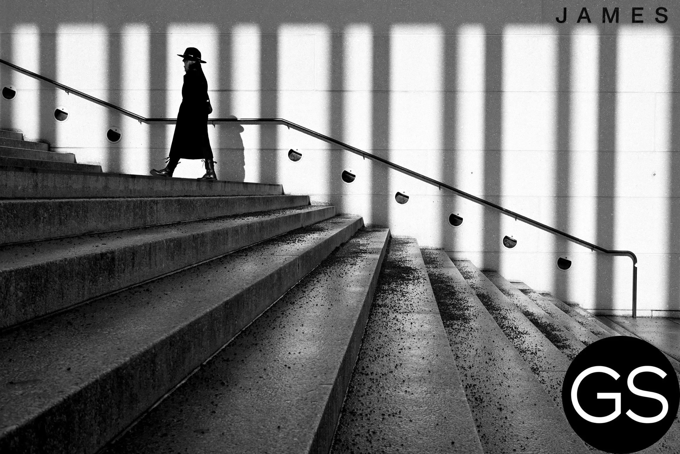 Schwarzweiß-Foto einer Person in einem Hut und Mantel, die einen Treppenabstieg macht, mit Wand im Hintergrund. Die Person ist in Seitenansicht und die Schatten werfen parallele Linien auf die Wand.
