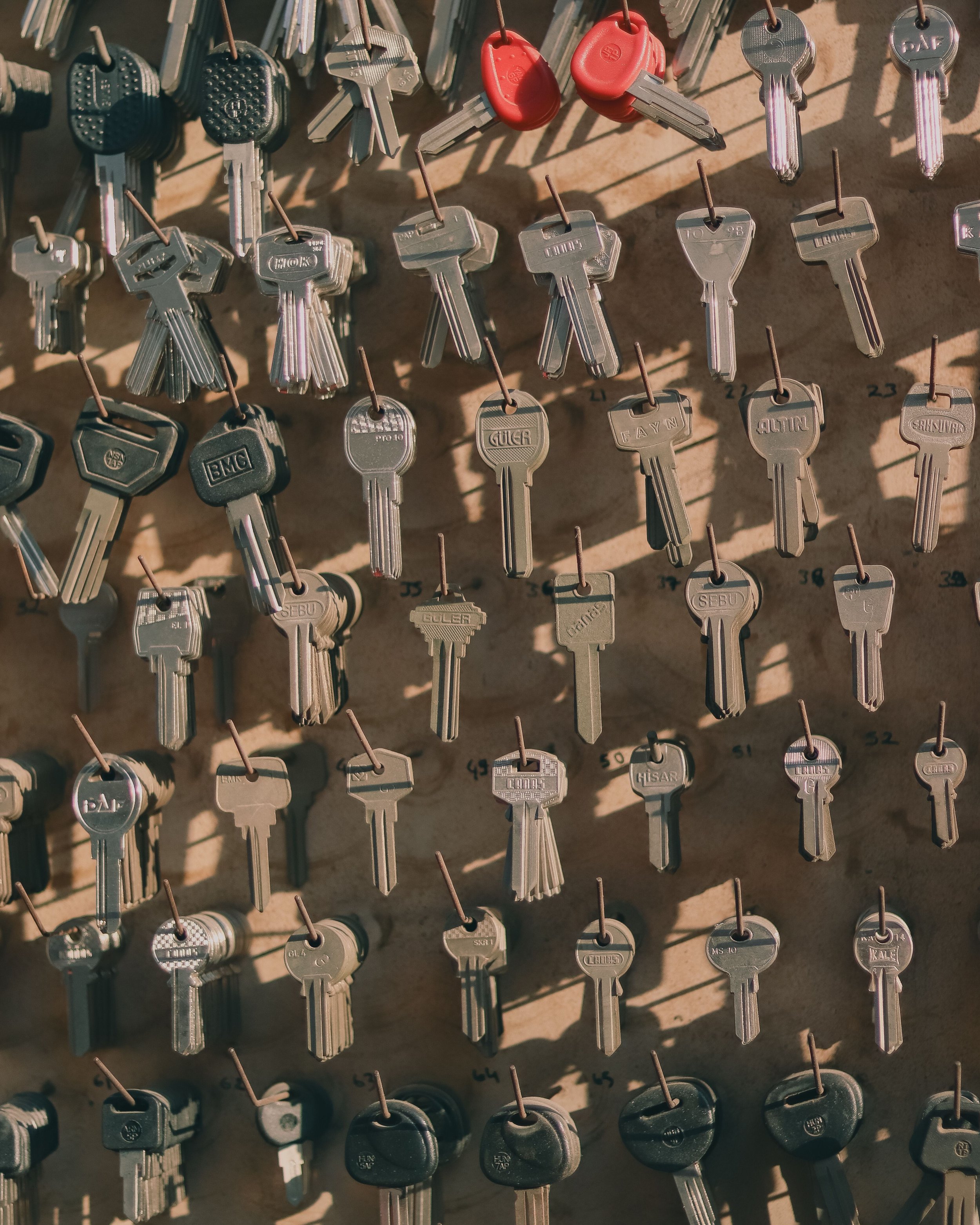 A wall display of various keys hanging on hooks, including silver keys and a few red keys, arranged in rows.
