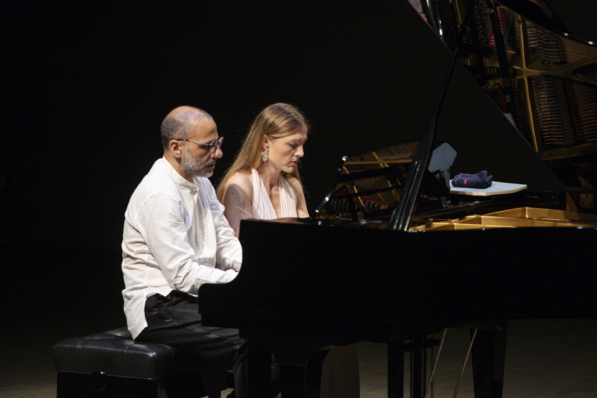 Costa & Casanova Piano Duo performing together at a grand piano on stage.
