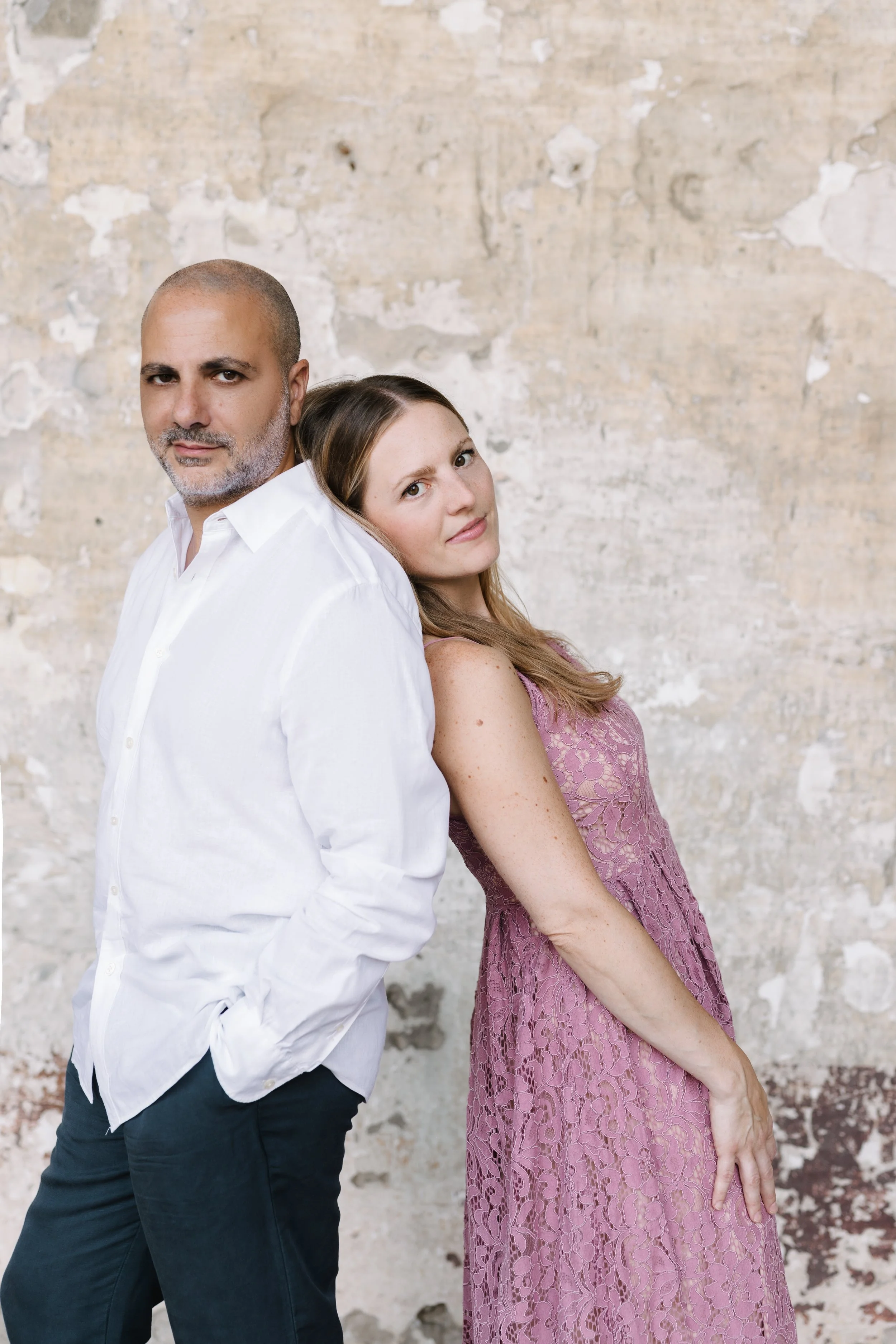 Sara Costa and Fabiano Casanova, Costa & Casanova Piano Duo, photographed from behind against a stone wall.