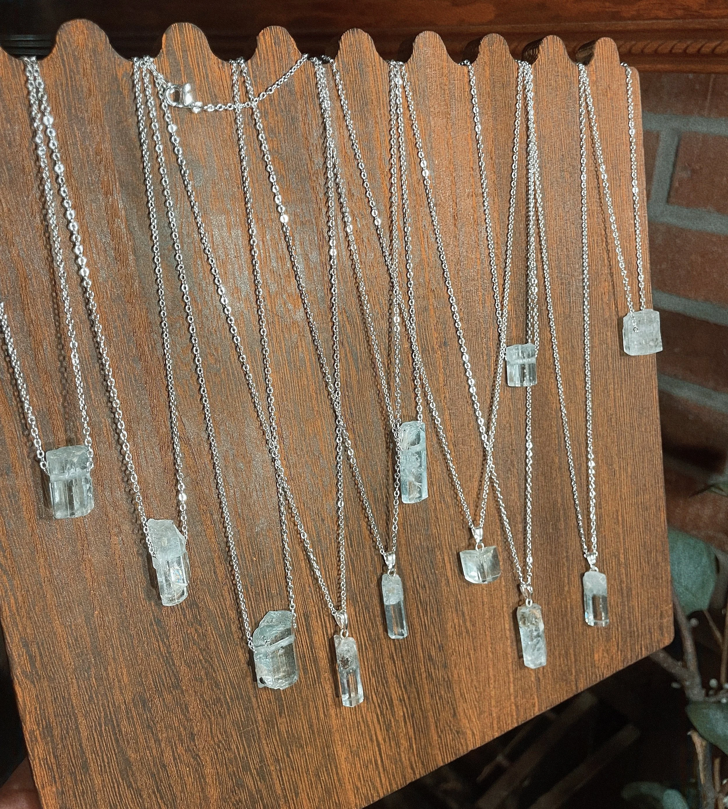 Multiple necklaces with clear rectangular pendants hanging on a wooden display.