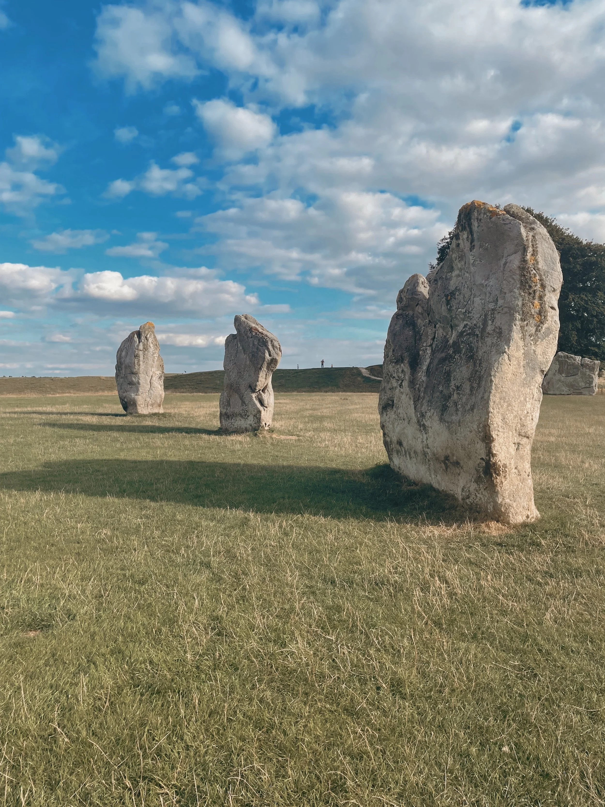 A landscape with four large standing stones on a grassy field, under a blue sky with scattered clouds.