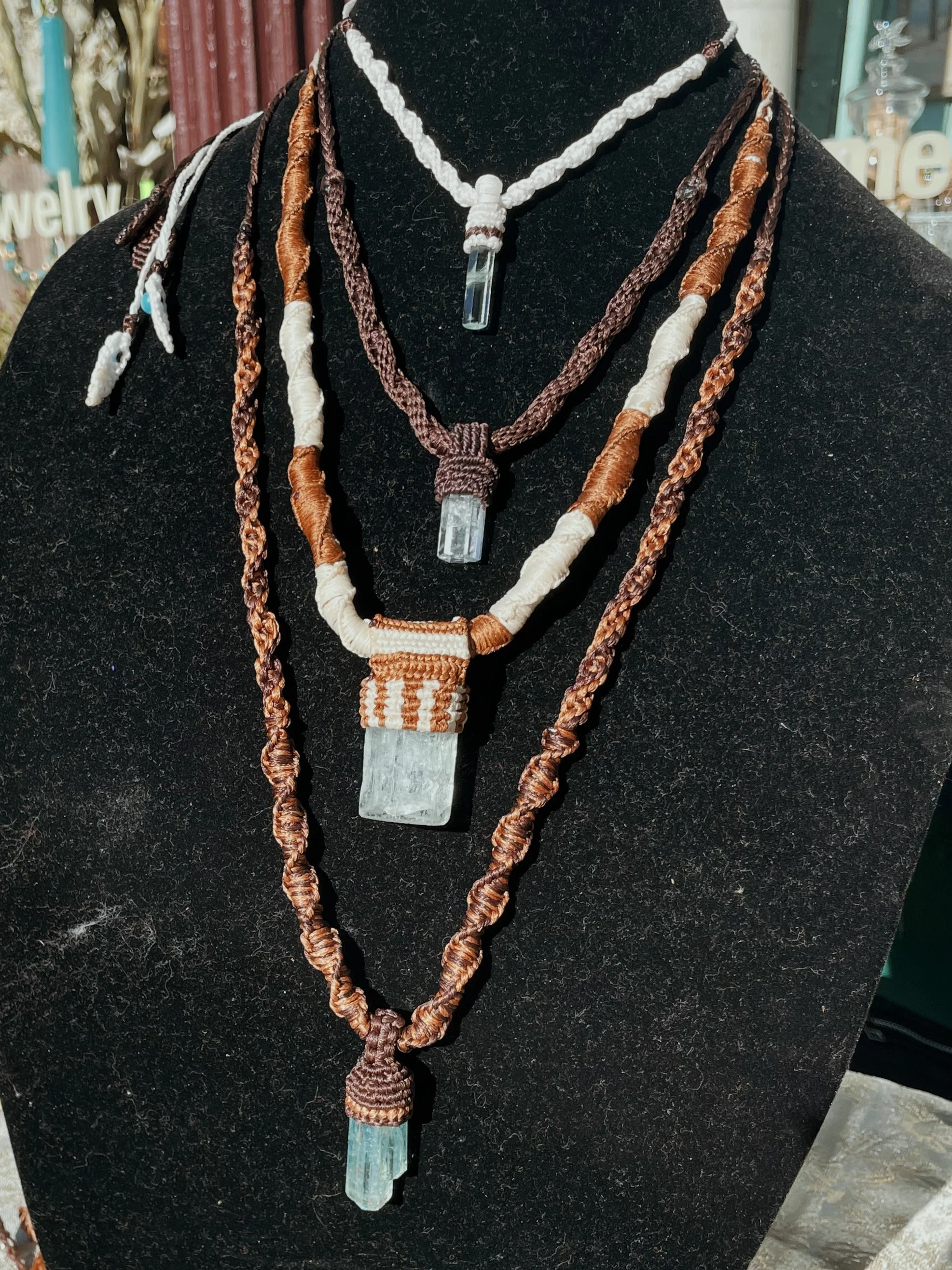 A display of woven jewelry necklaces with large crystal pendants, arranged on a black background.