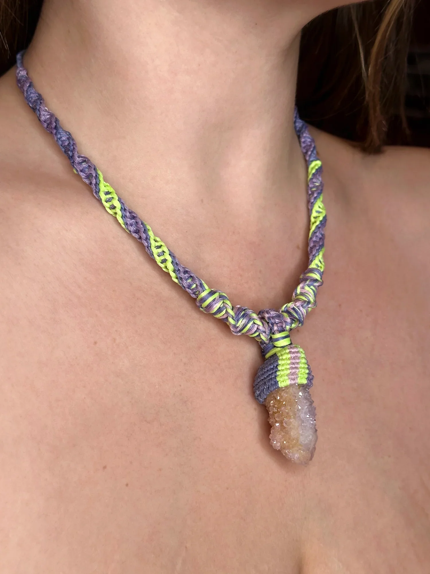Close-up of a necklace with a large, rough, brownish-orange crystal pendant wearing on a person’s neck and chest.