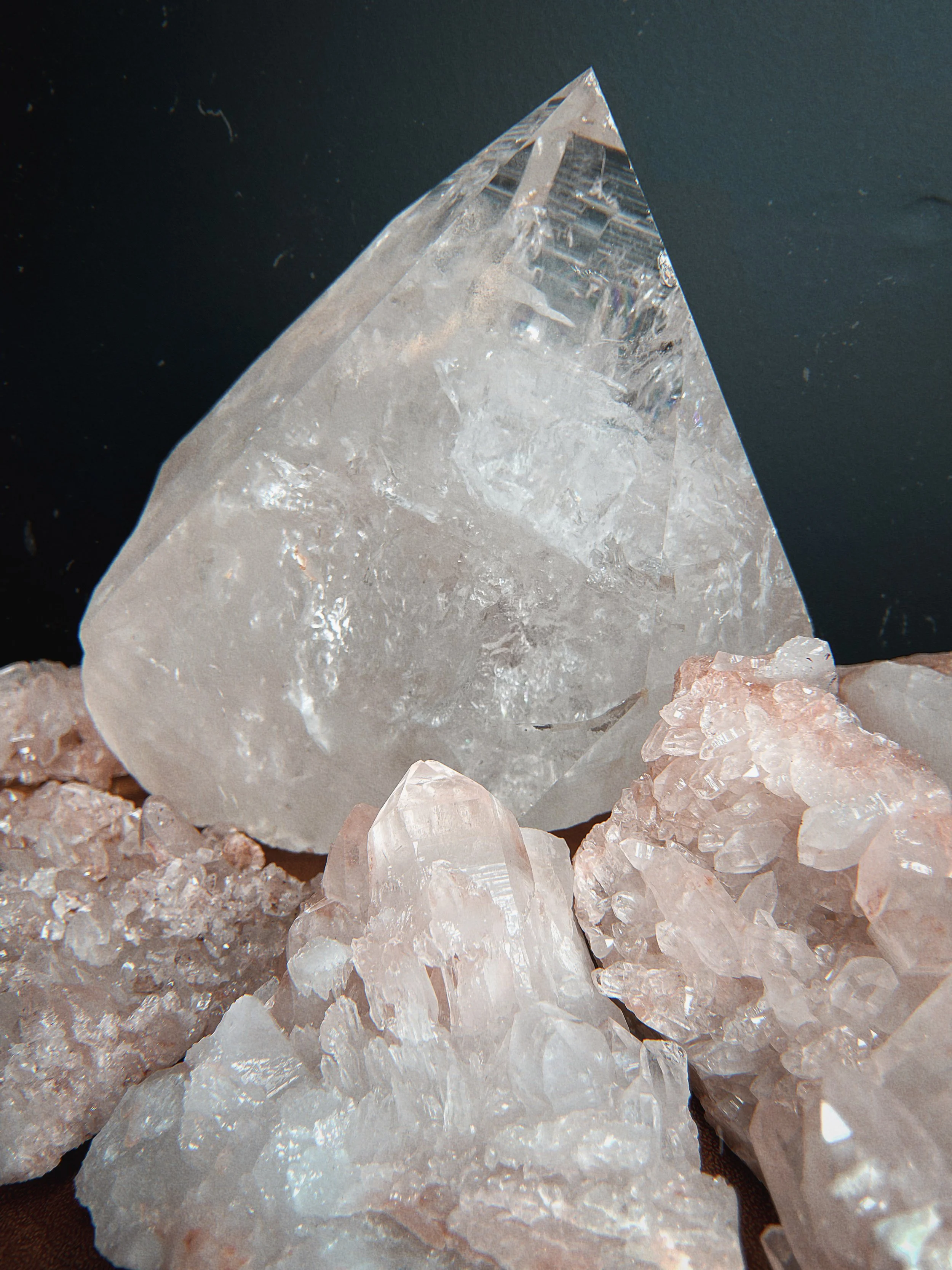 Close-up of a large, clear quartz crystal surrounded by smaller quartz crystals with a dark background.