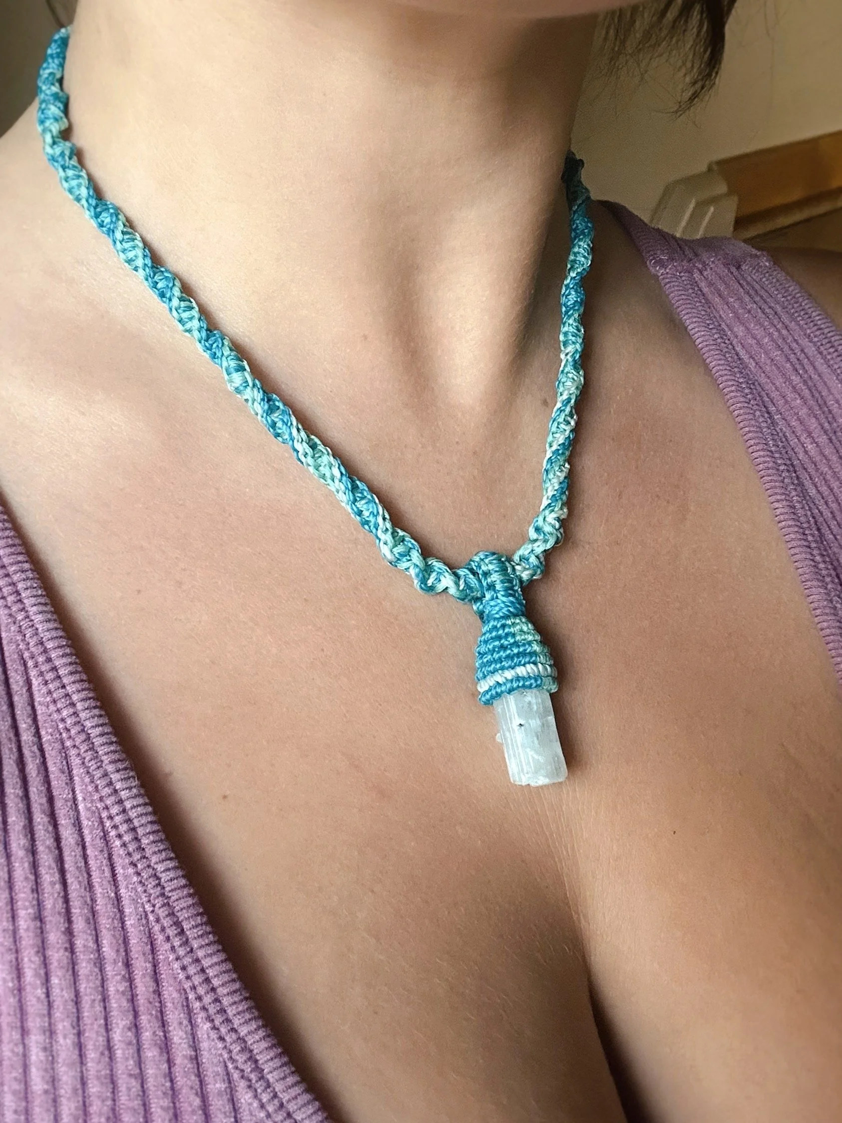 A close-up of a person's neck and chest area showing a blue and white twisted cord necklace with a clear pendant.