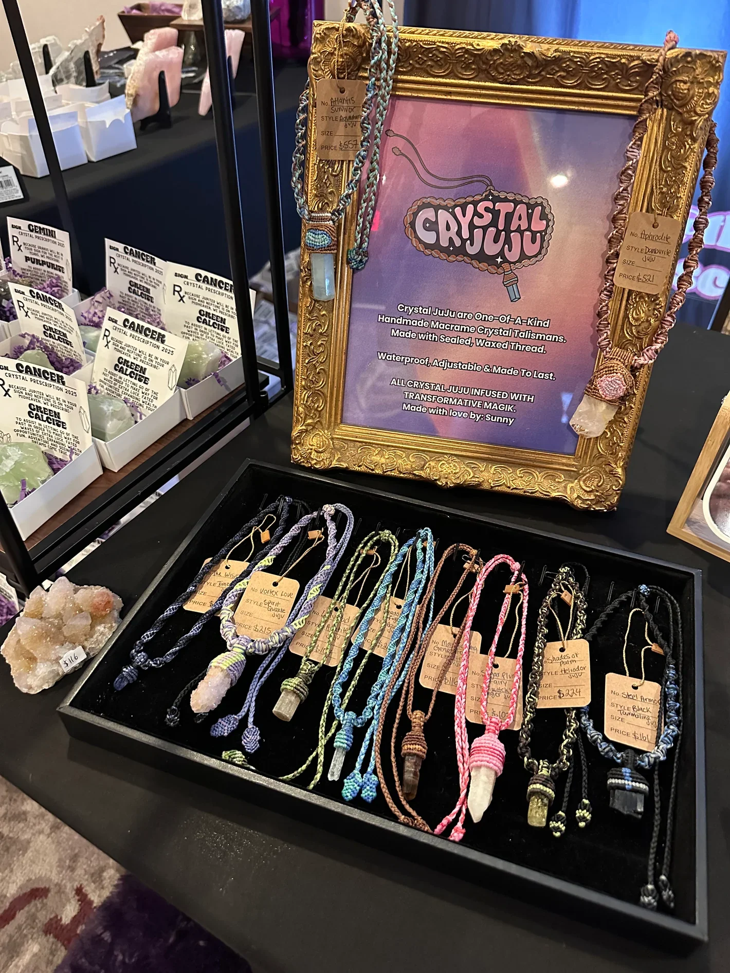 Display of handmade macrame crystal necklaces with colorful braided cords and stone pendants at a jewelry booth.
