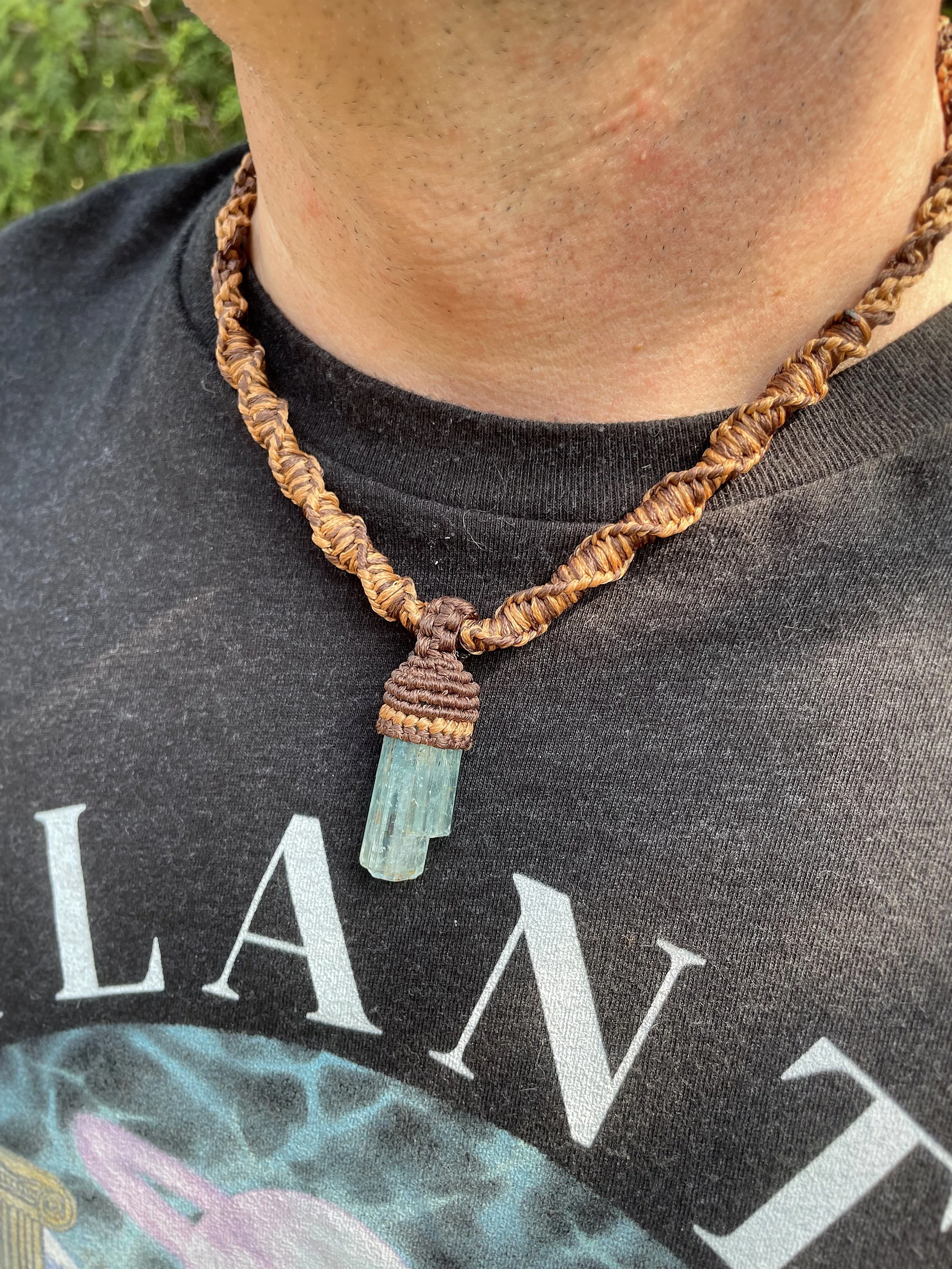 Close-up of a person's neck wearing a dark T-shirt and a handcrafted necklace with a large green crystal pendant.