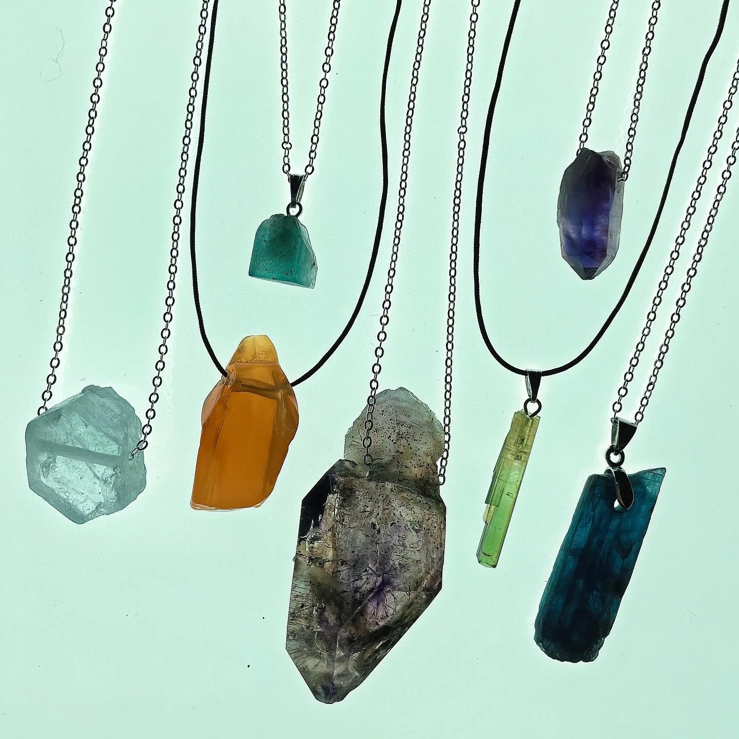 Necklaces with large, colorful pendants made of various stones and crystals hanging against a light background.