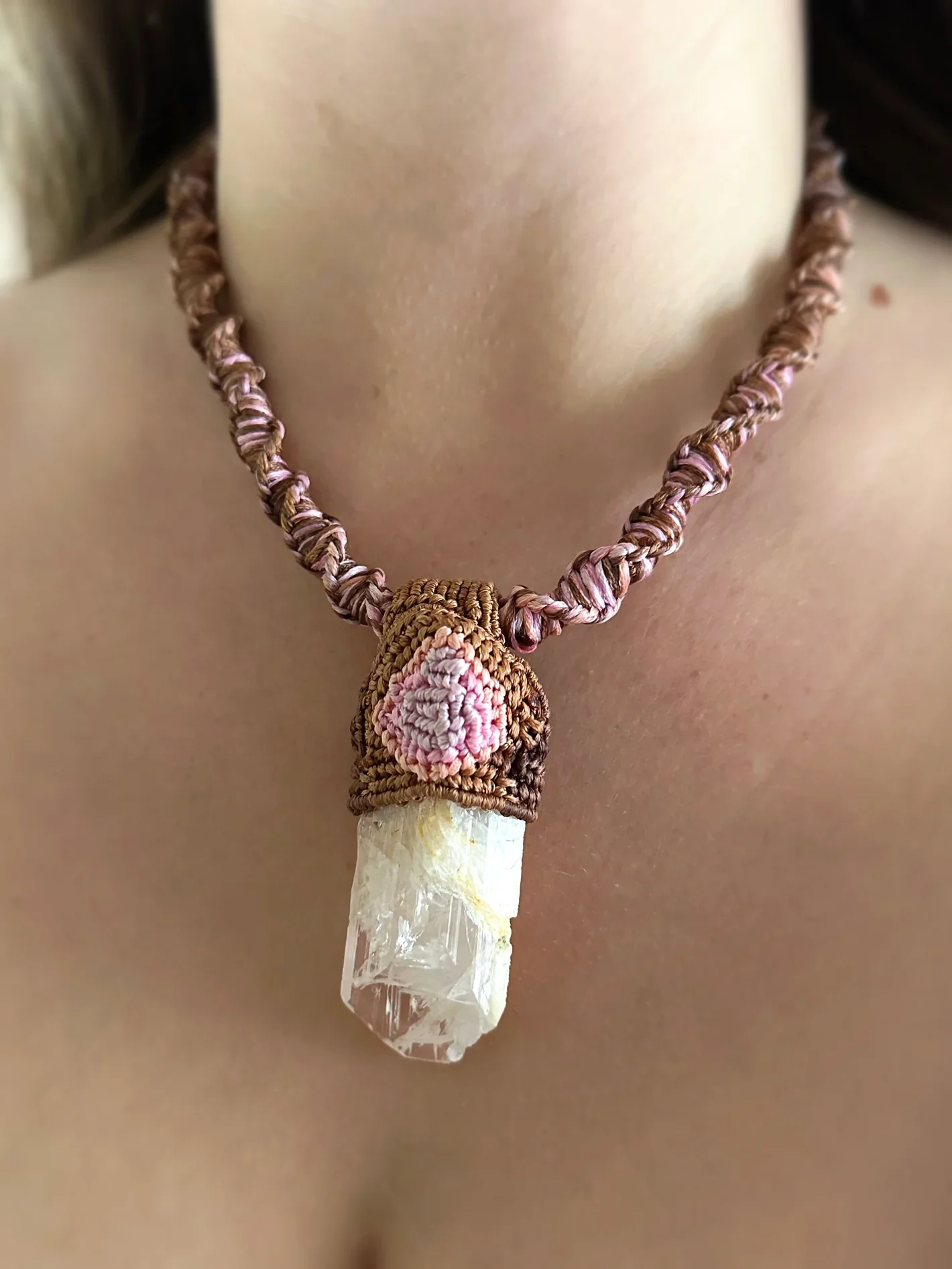 A necklace with a large clear crystal pendant wrapped in brown, pink, and beige braided cords.