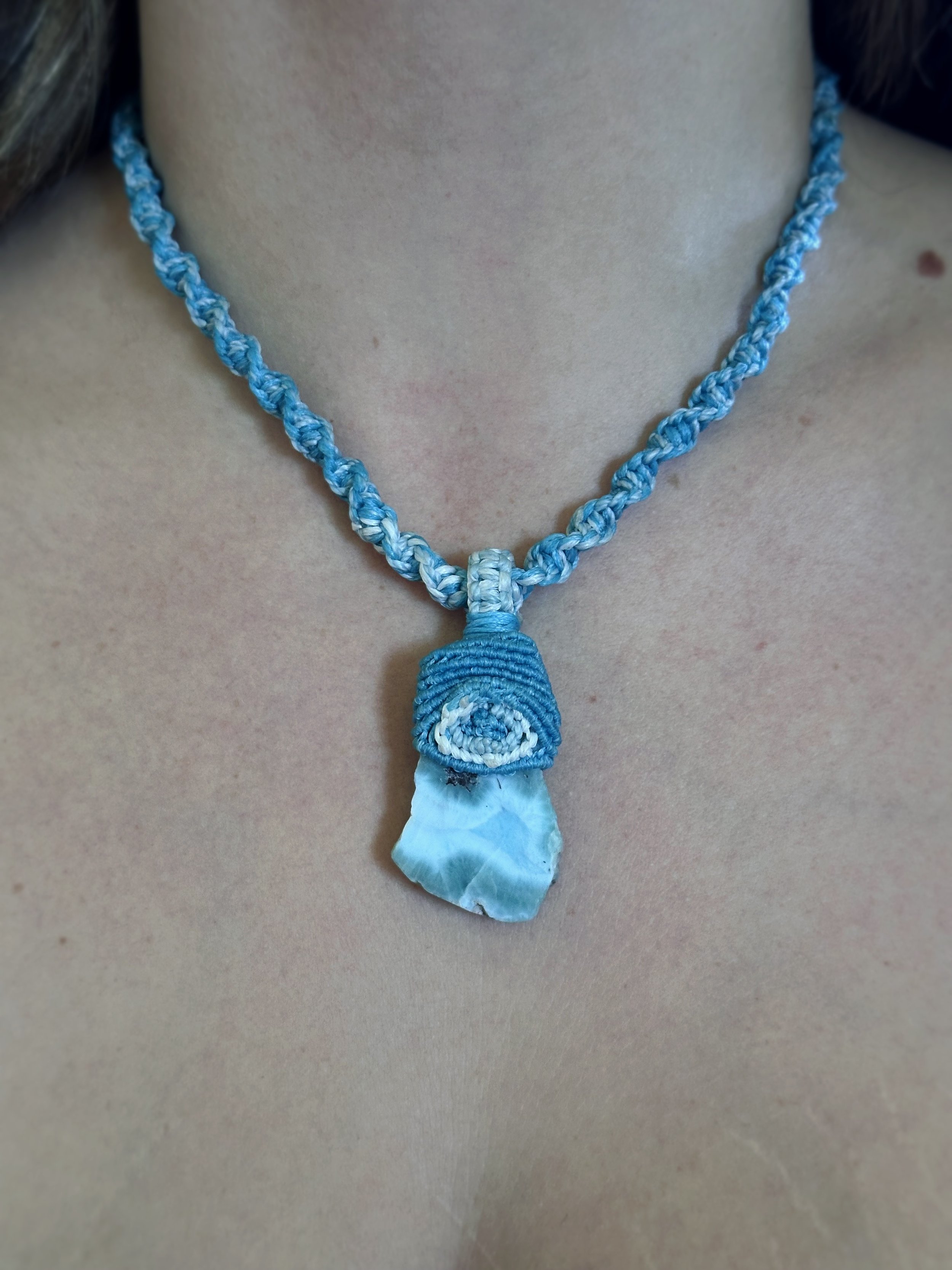 A blue woven necklace with a spiral pendant and a piece of blue and white fabric hanging from it.