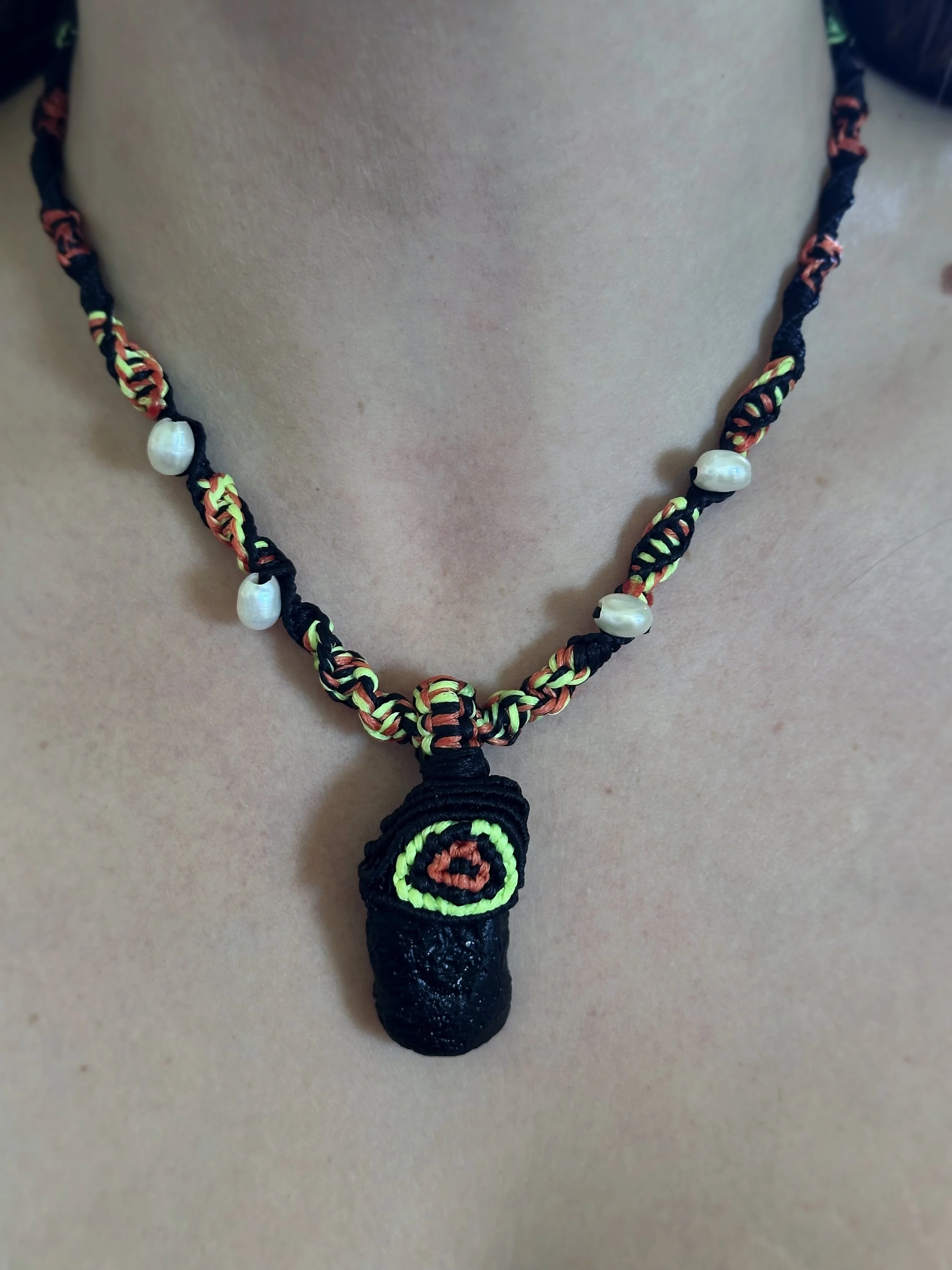 Close-up of a person wearing a handmade beaded necklace with shells and a woven pendant.