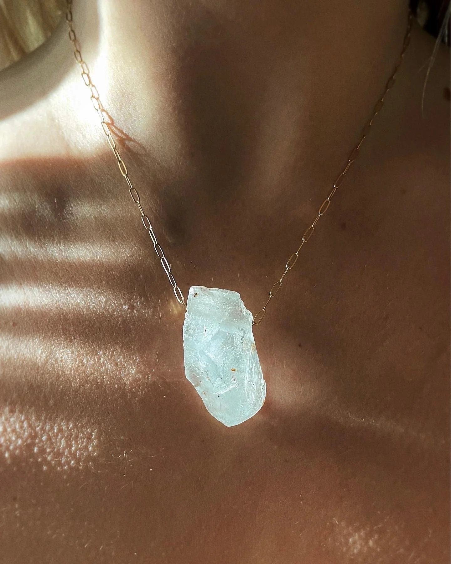 Close-up of a person's neck and chest, showing a gold chain with a large white crystal pendant.