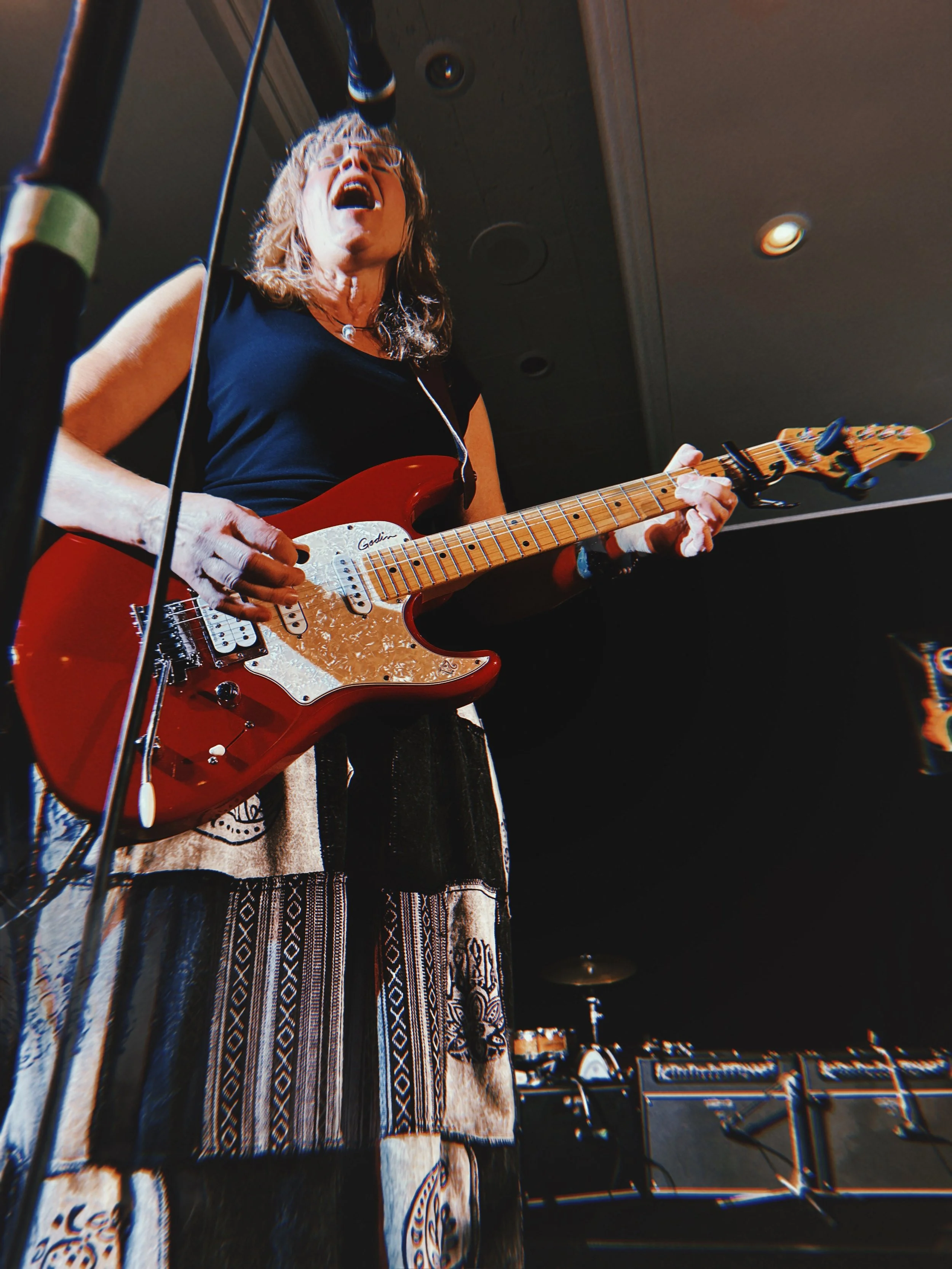 Female musician singing and playing an electric guitar on stage.