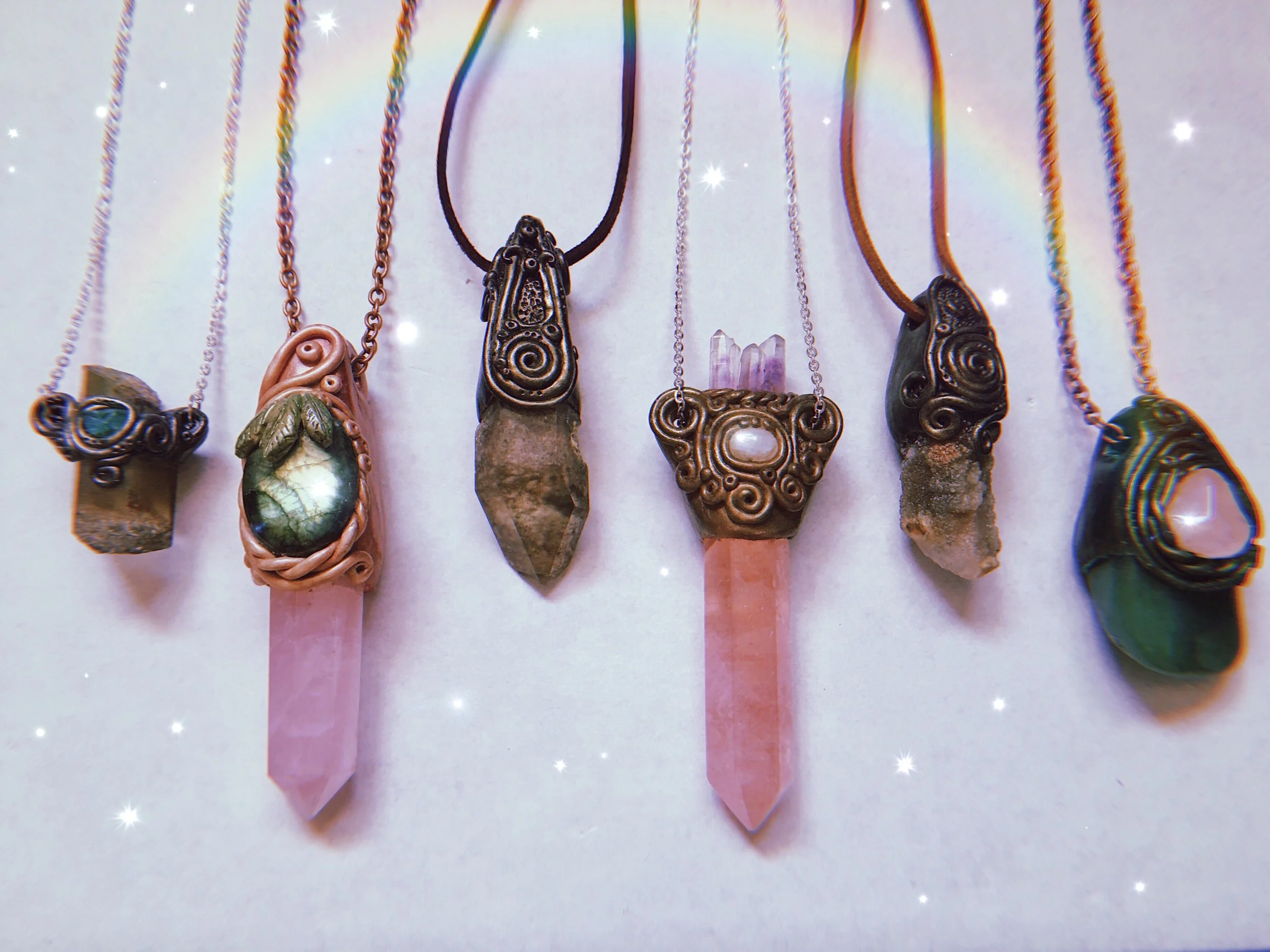 Collection of necklaces with various pendant stones and designs, hung on display against a light background with sparkles.