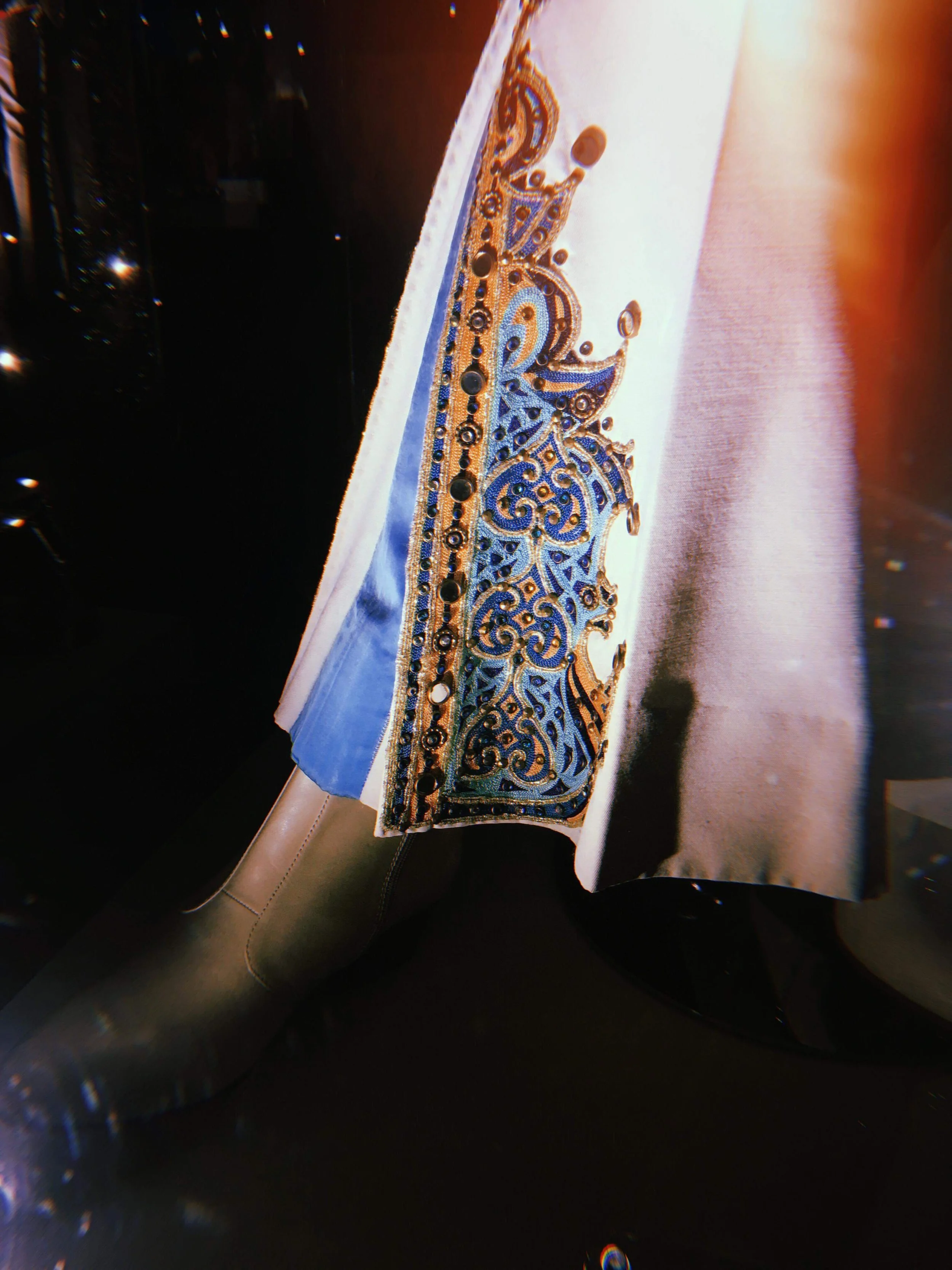Close-up of intricate embroidery with blue, gold, and black thread on a fabric, possibly part of a decorative garment or textile art.